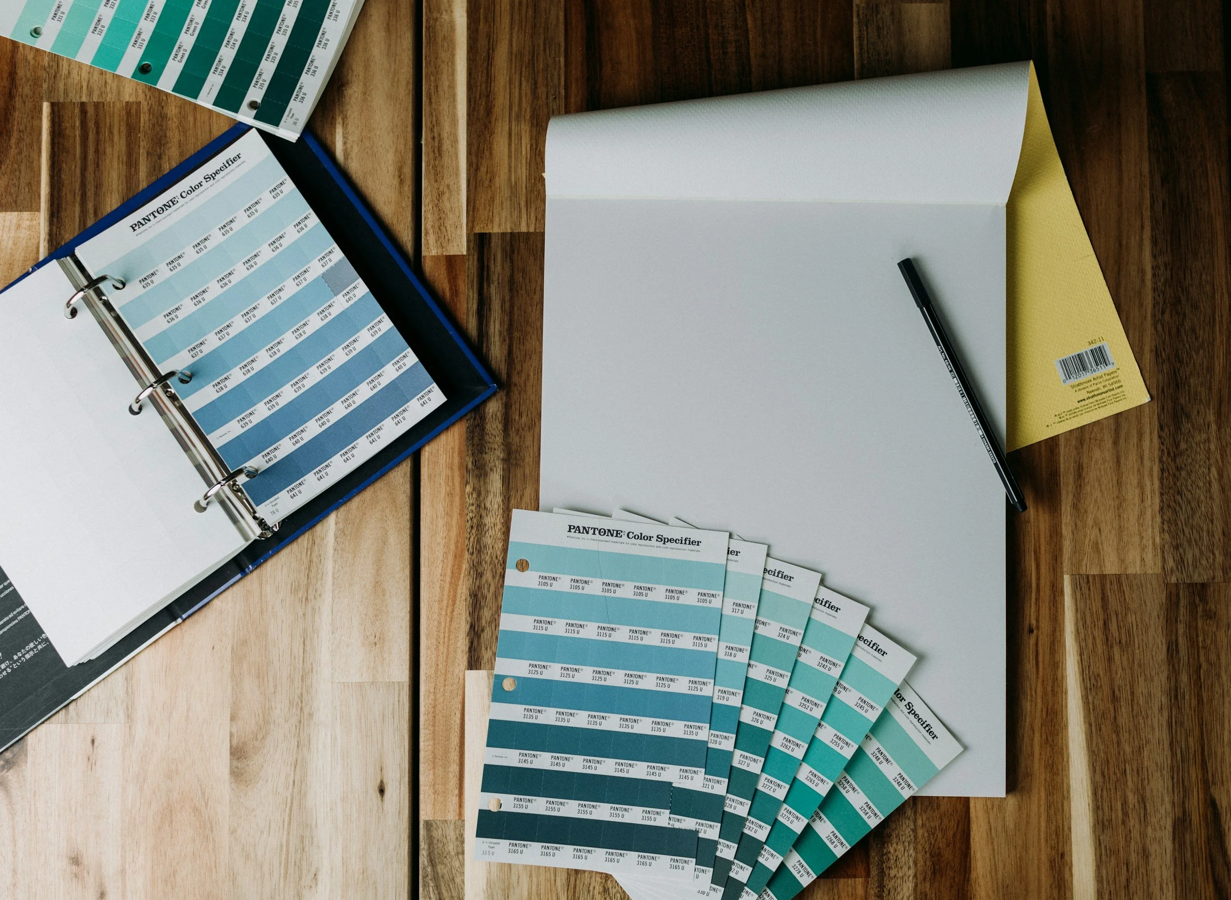 Color swatches, a color guide book, and sheets with Pantone color samples on a wooden table.