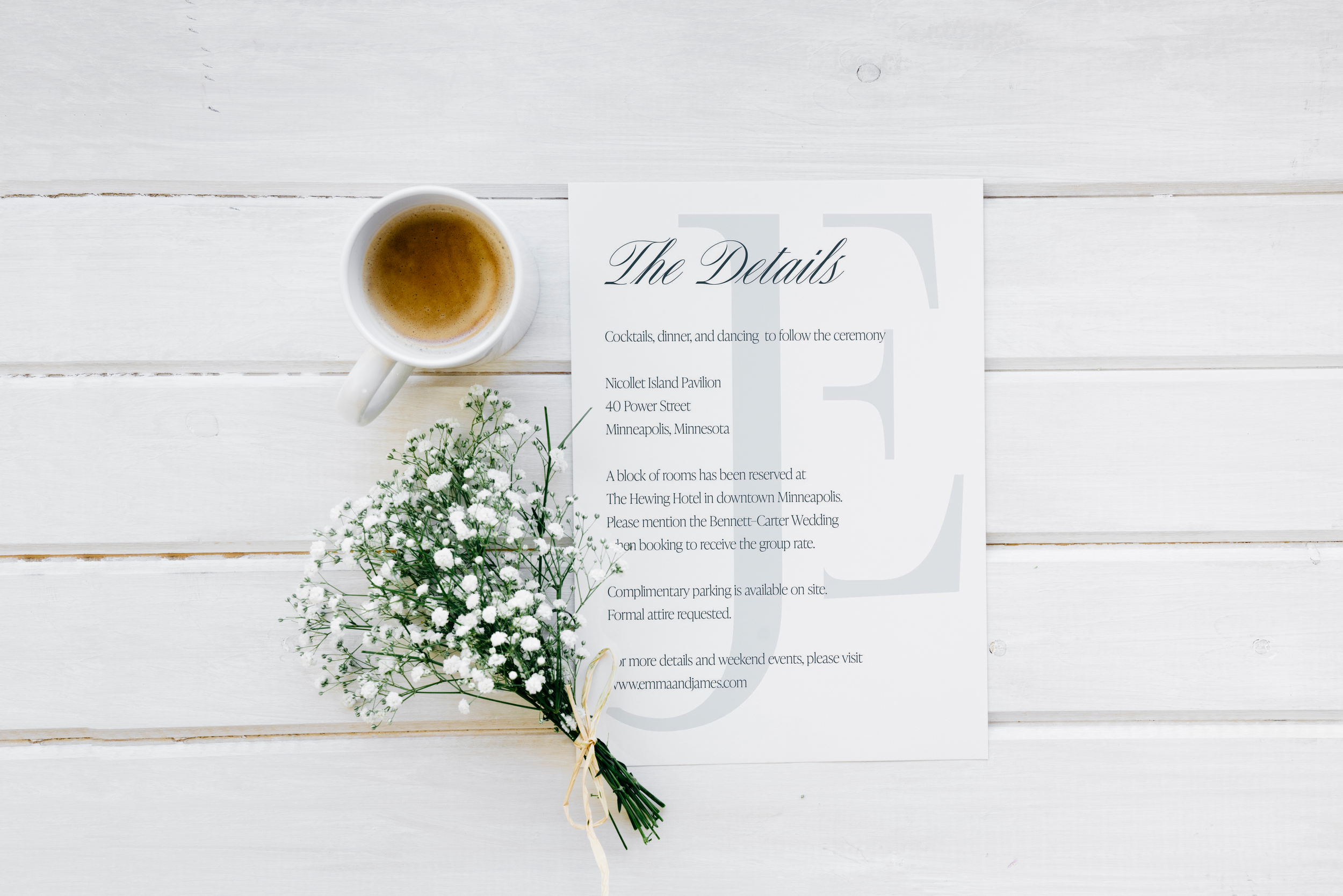 A white coffee mug filled with coffee, a white bouquet of small white flowers tied with a ribbon, and a wedding ceremony program on a white wooden surface.