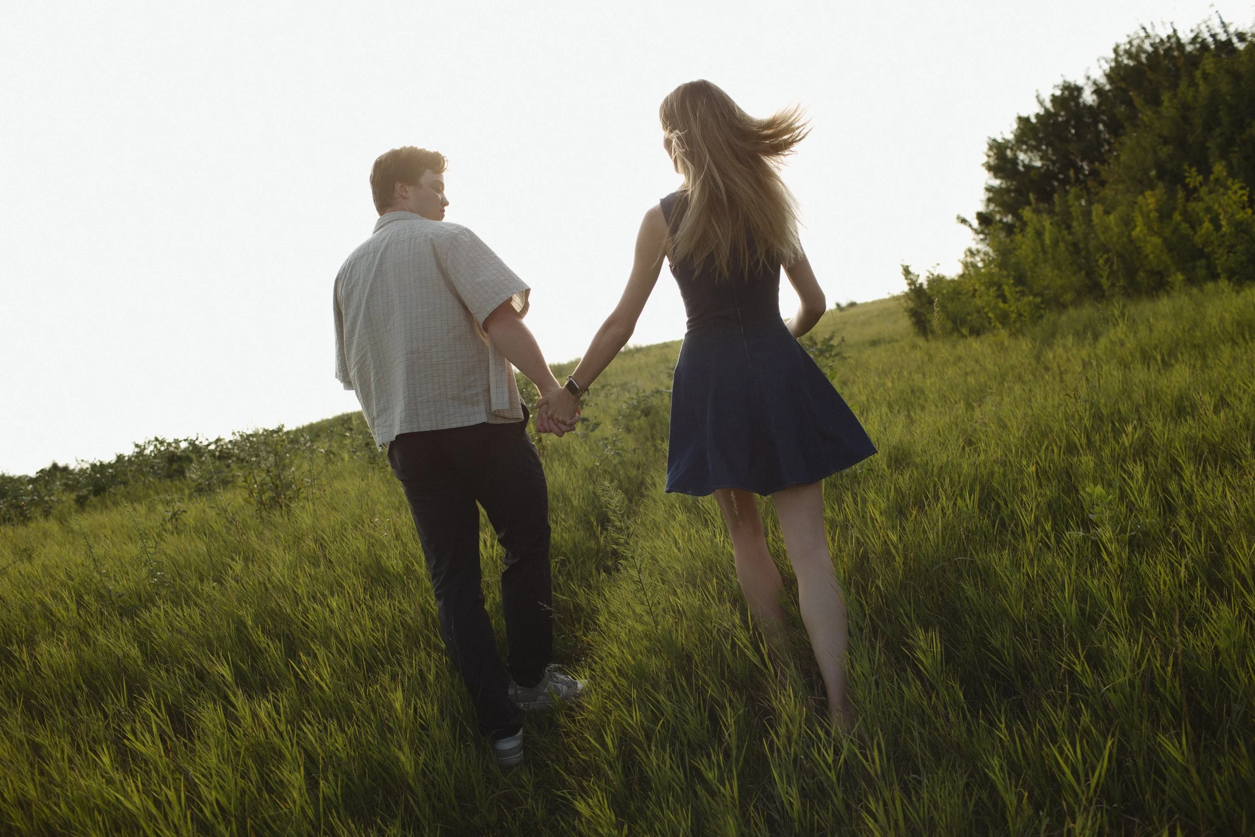 A young couple holding hands and walking through a grassy field.