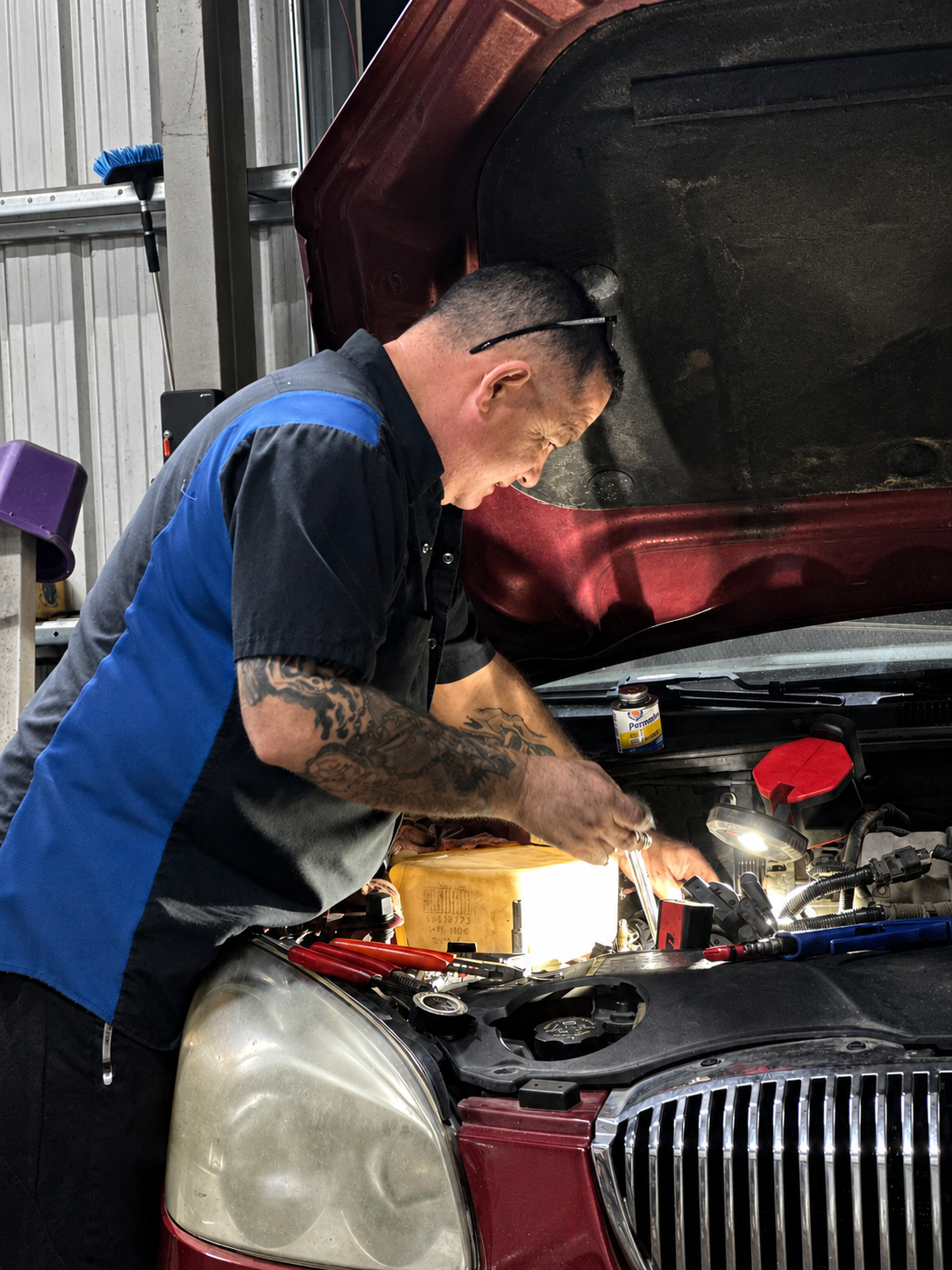 A mechanic working on a car engine with the hood open, using tools in a garage.