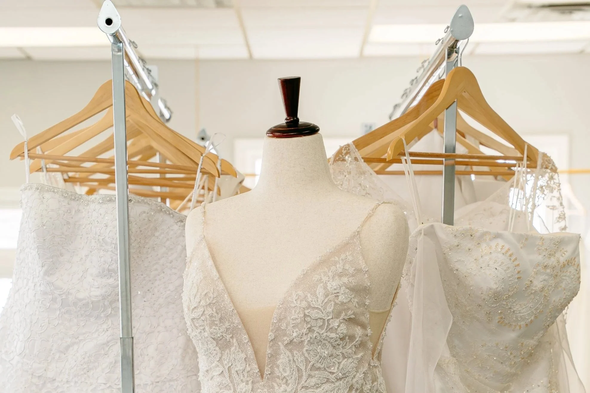 Professional photo of mannequin in front of racks of wedding gowns.