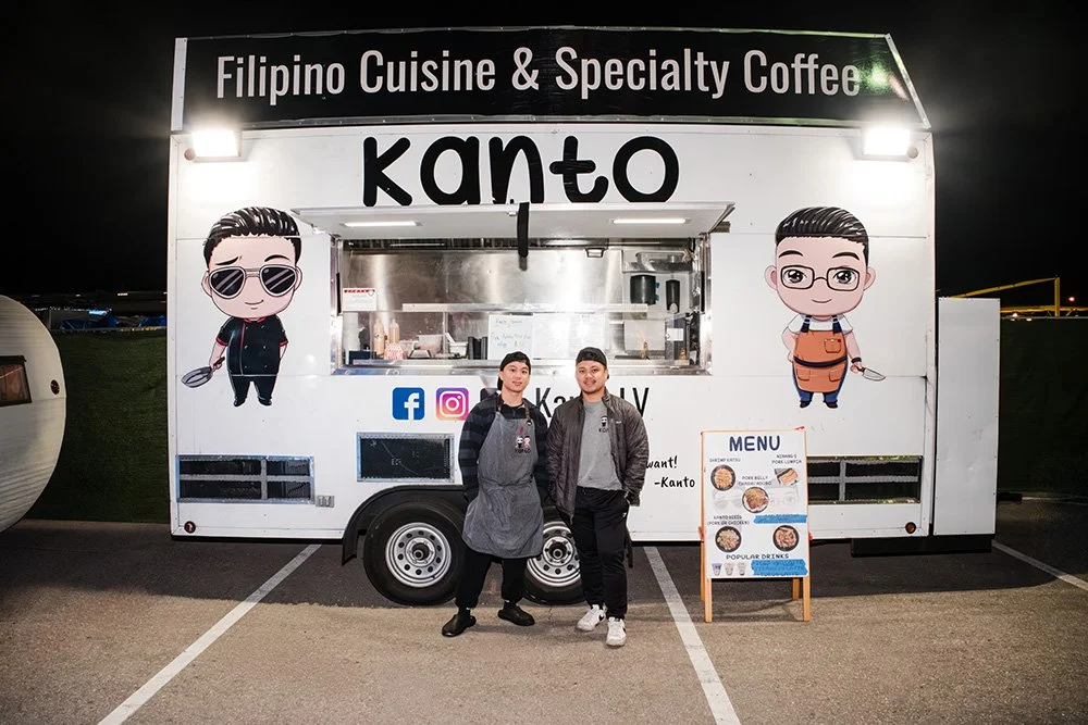  Filipino food truck named Kanto selling Filipino cuisine and specialty coffee, with two people standing in front, a menu board, and cartoon character illustrations on the truck.