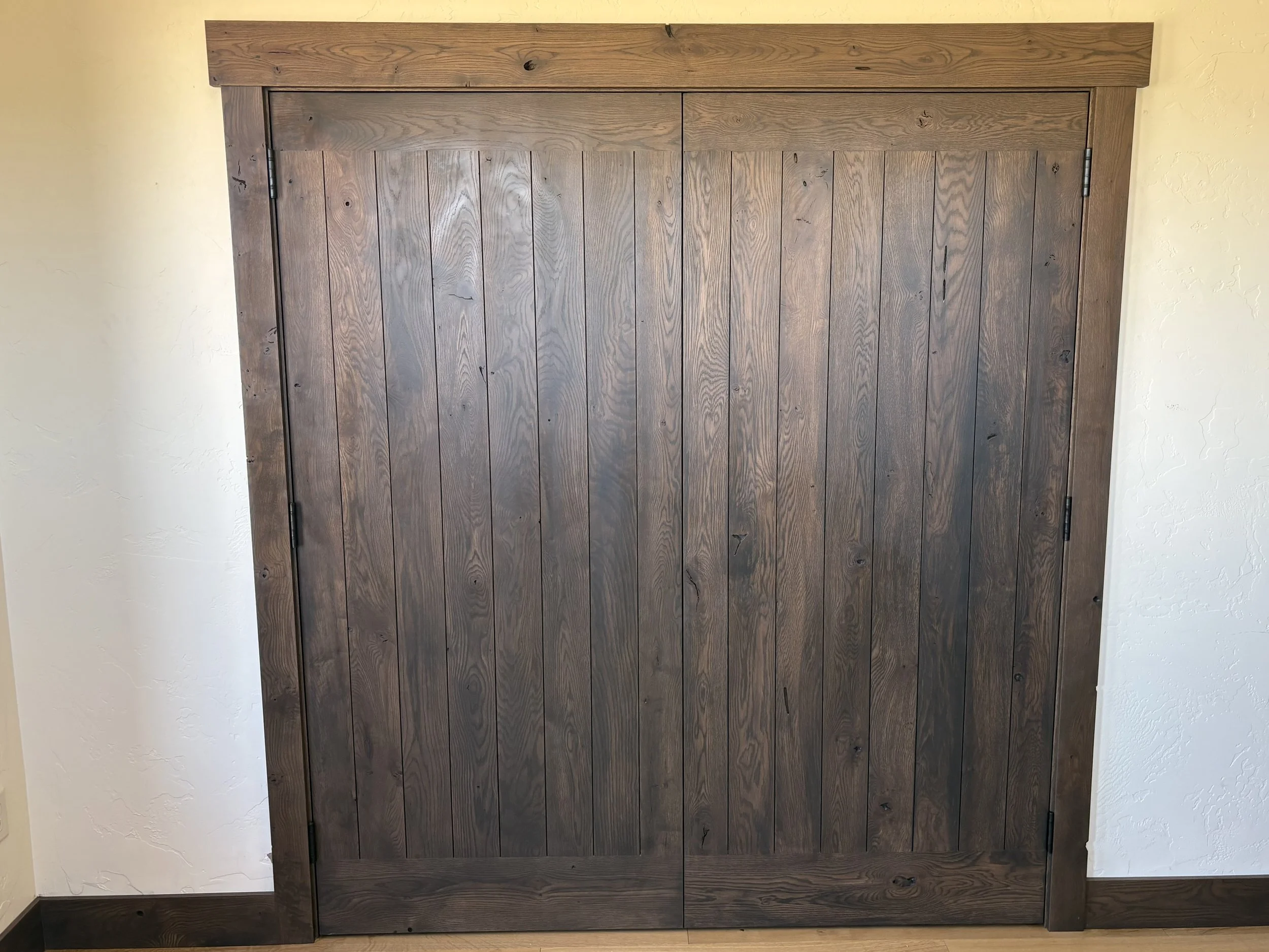 A wooden barn door with vertical planks, mounted on black hinges, set within a light yellow wall.