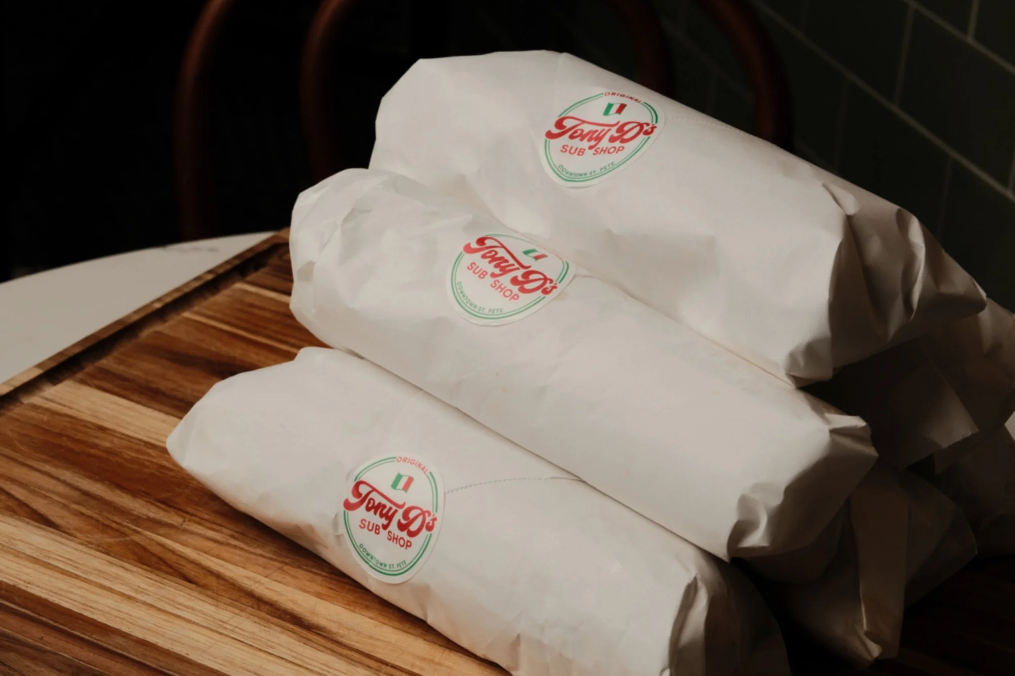 Three wrapped sub sandwiches with Tony D's Sub Shop logo sitting on a wooden table.