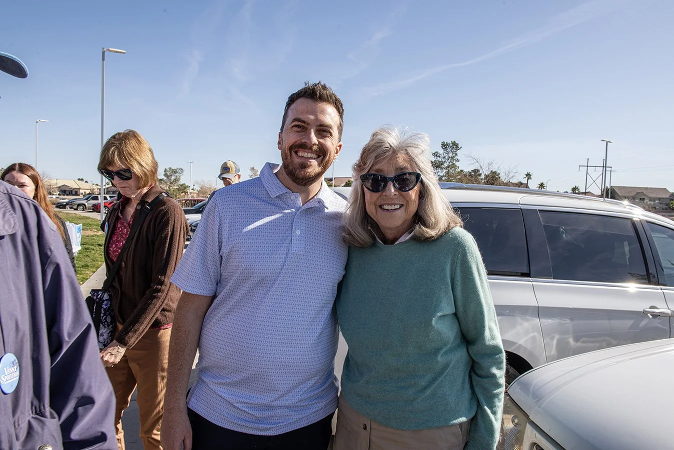 Vinny Spotleson and Dina Titus smiling and posing together outdoors with cars and other people in the background.
