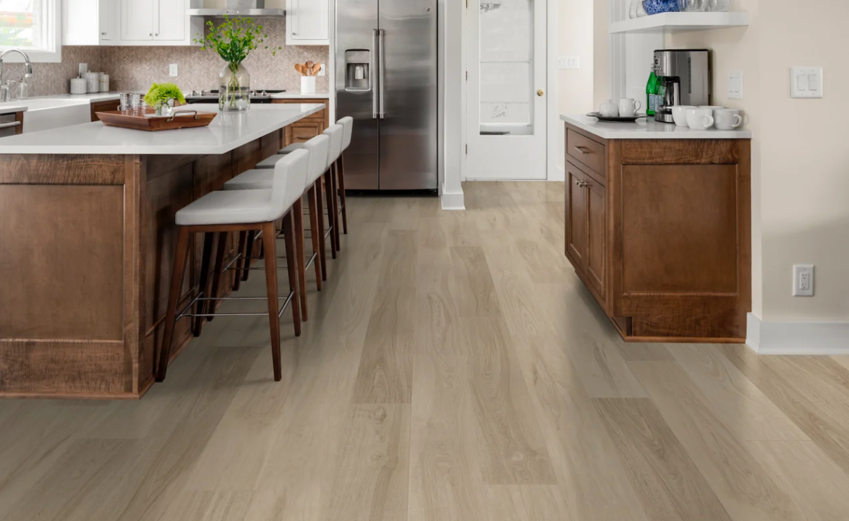 A kitchen with a light wood floor, white countertops, wooden cabinets, a stainless steel refrigerator, and a small counter with a coffee maker and cups.