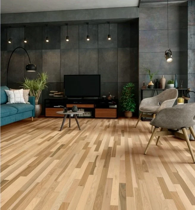Living room with grey wall, wooden floor, blue sofa, beige armchairs, black TV on a stand, small coffee table, and various plants and decor.
