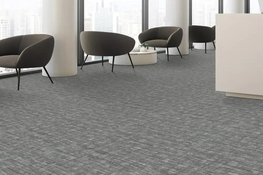 Modern office waiting area with gray carpet, black chairs, and large windows showing city buildings