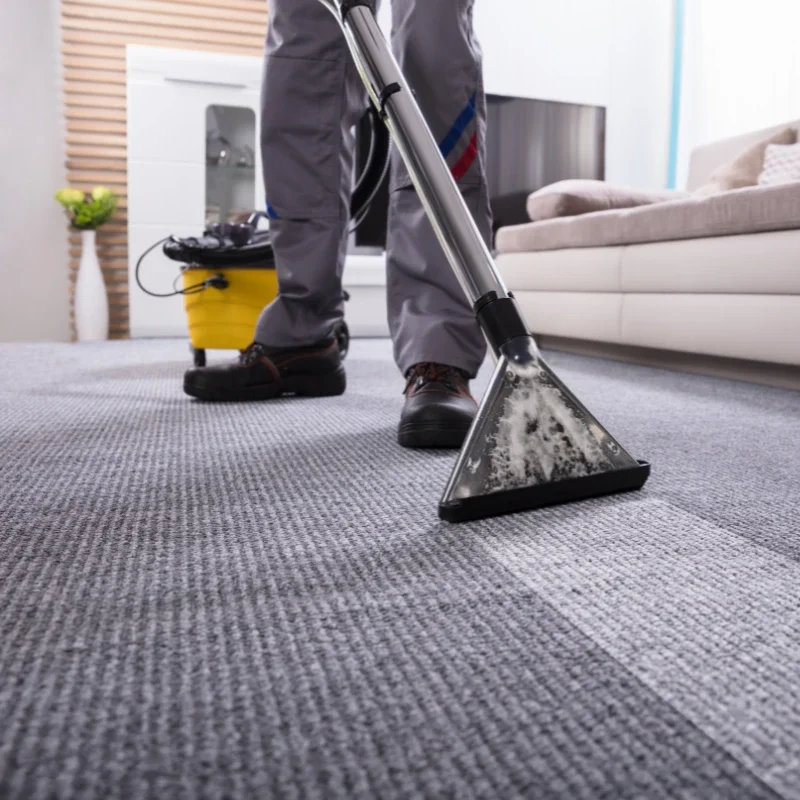 Person vacuuming a gray carpet in a living room with a handheld vacuum cleaner.