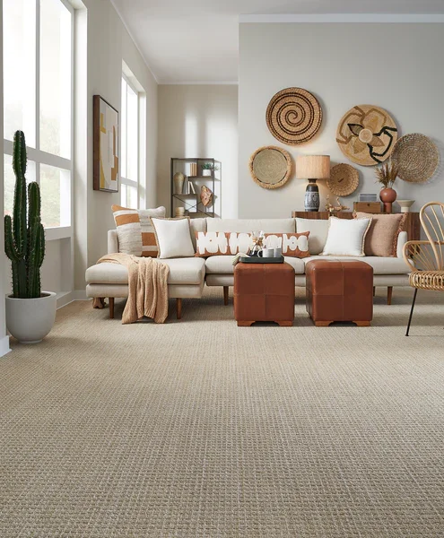 Living room with white sofa, decorative pillows, two brown ottomans, a rattan chair, and wall art with woven baskets.