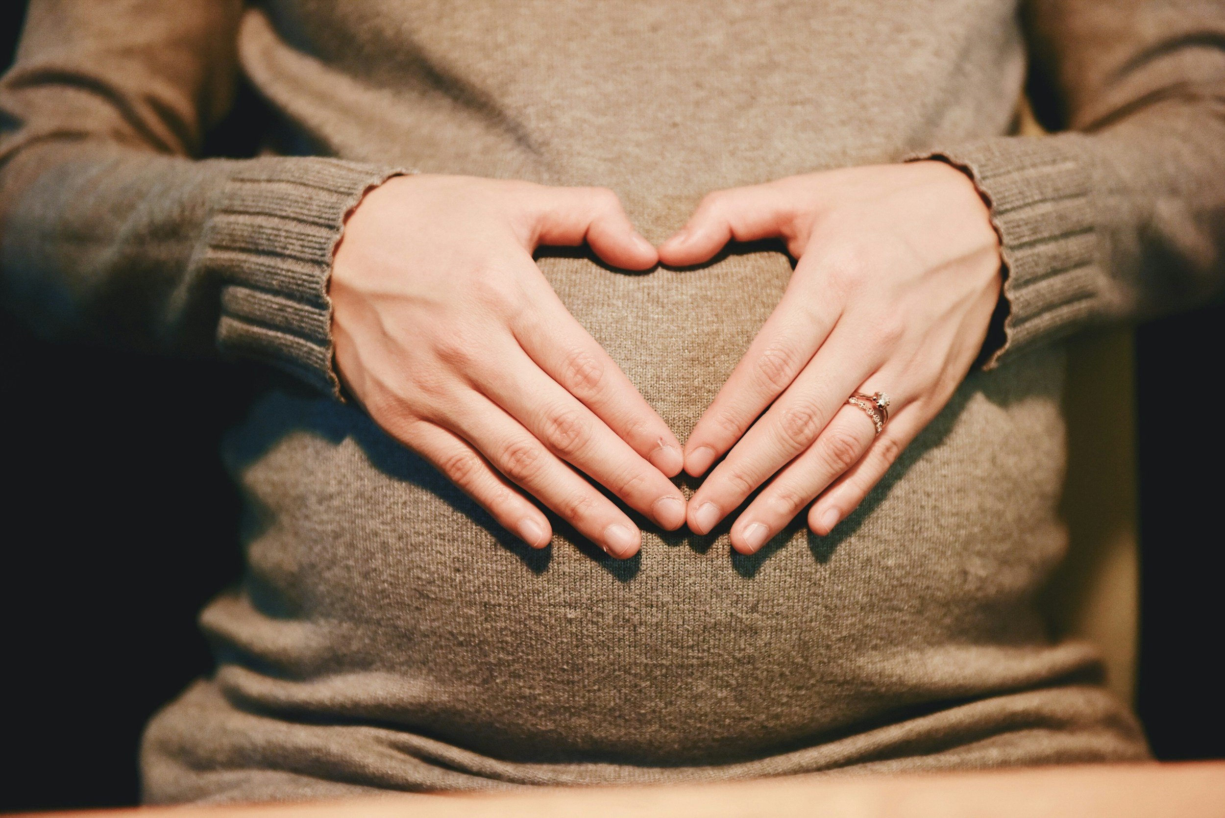 Hands forming a heart shape over a pregnant belly