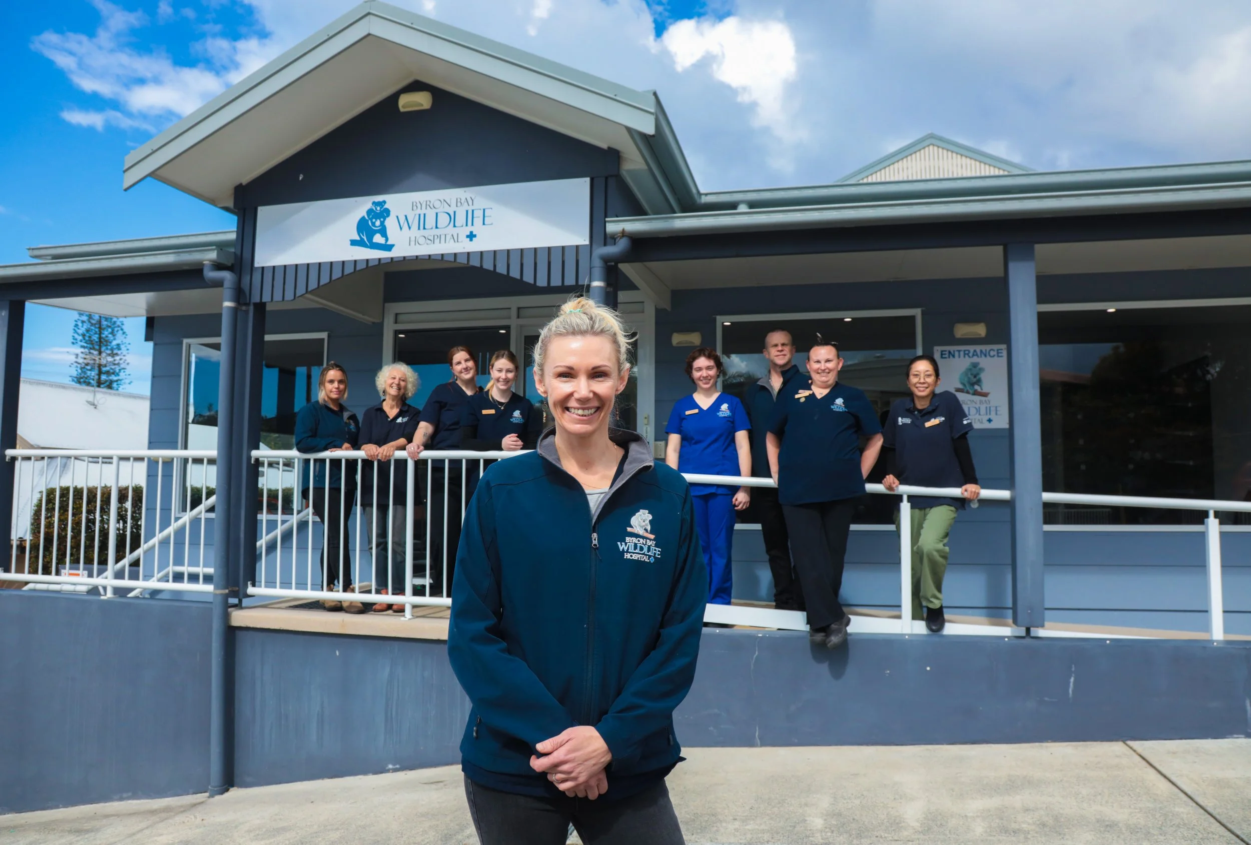 A group of nine staff members and volunteers standing and sitting outside the Byron Bay Wildlife Hospital, with General Manager of Veterinary Services Dr Bree Talbot in the front smiling at the camera, in front of the hospital building.