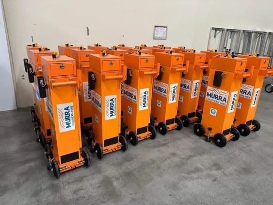 A row of orange floodlights on wheels lined up in an indoor storage area.