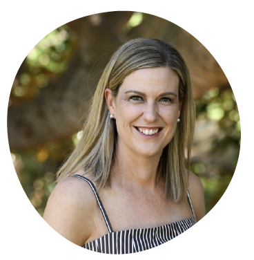 A woman with blonde hair smiling outdoors, wearing a sleeveless striped top.