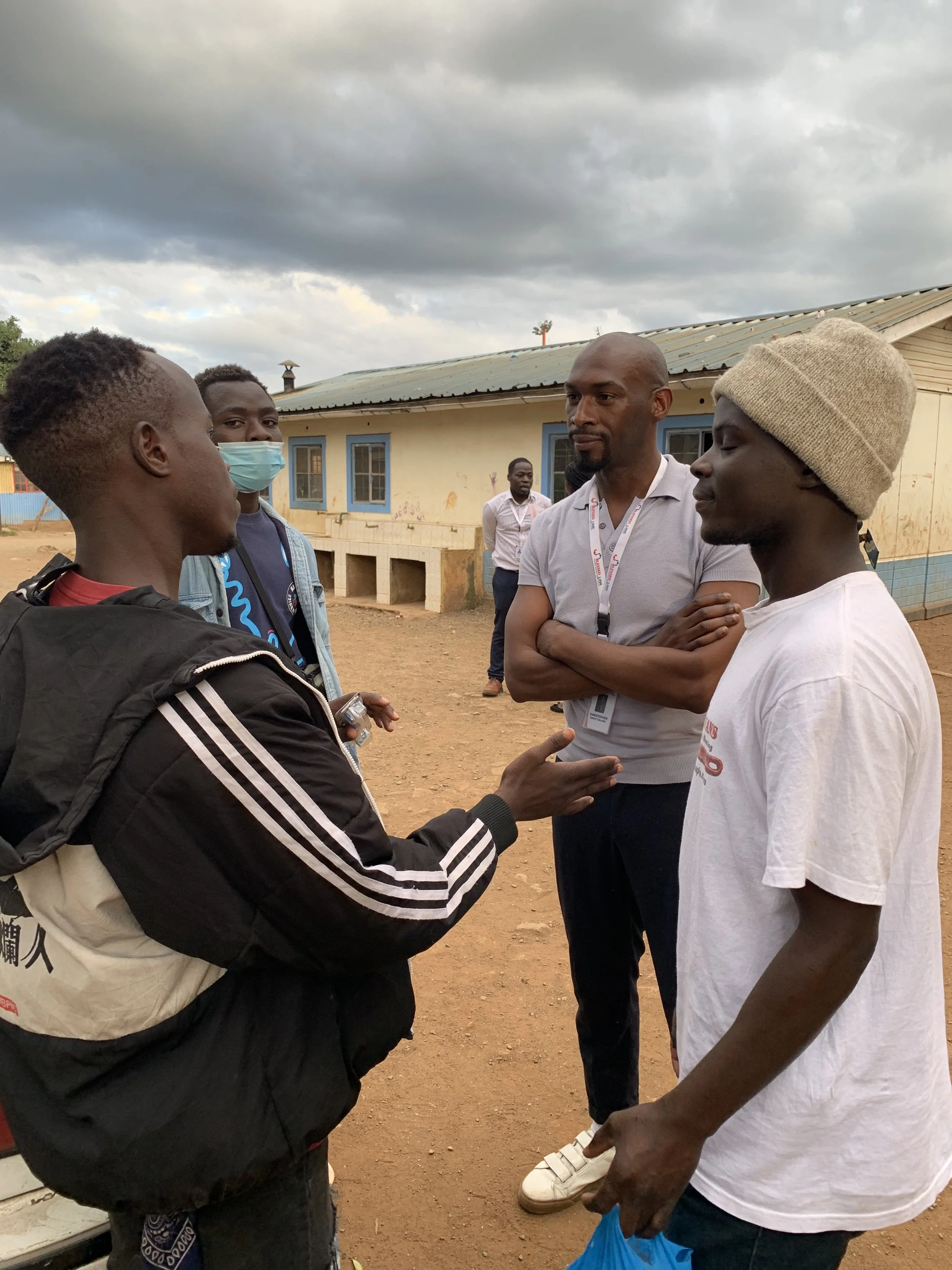 Group of five men having a conversation outside a building with a cloudy sky overhead.