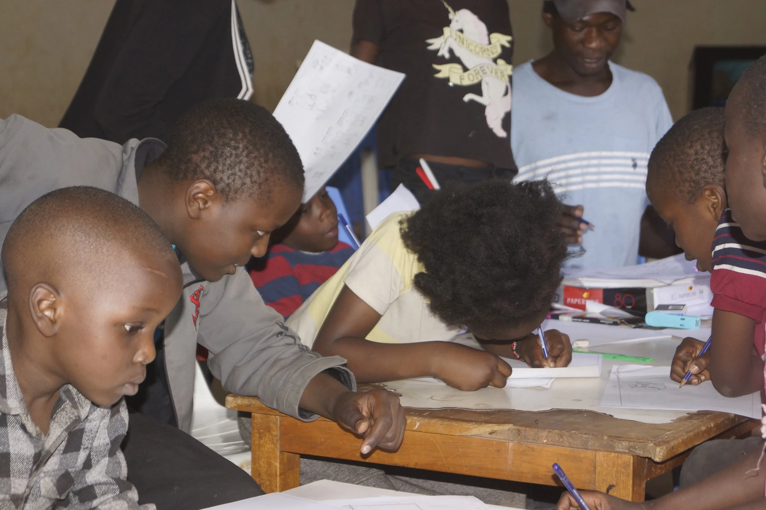 Children and adults gathered around a table, actively writing or drawing on paper.