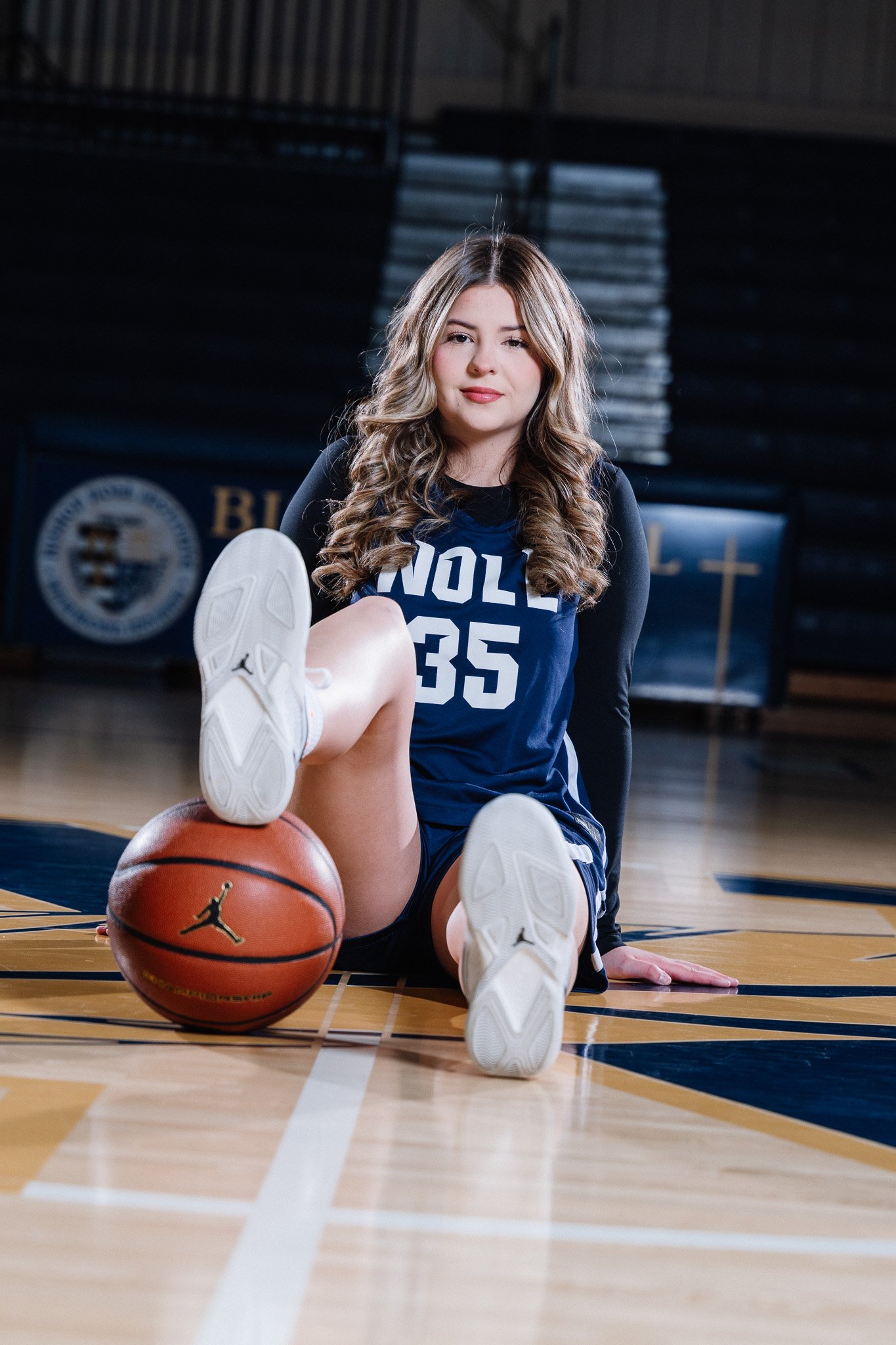 Young woman in athletic uniform sitting on basketball court with a basketball.