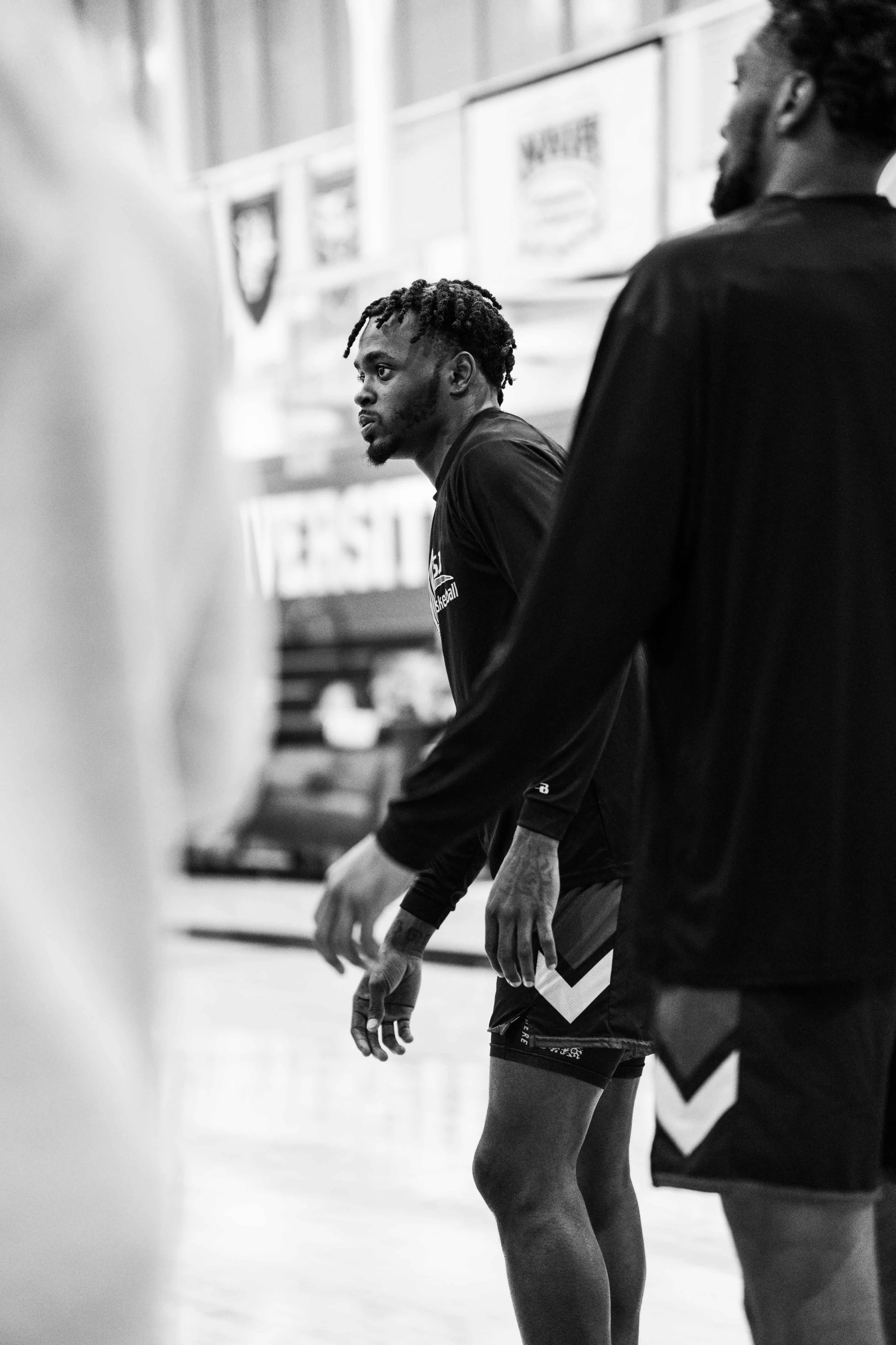 A group of men in sportswear standing in a gymnasium, with one man in the middle looking to the side, in black and white.