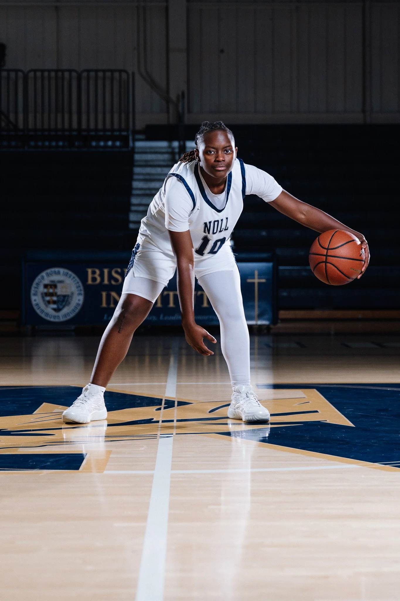 A female basketball player in a white uniform with the number 10, dribbling a basketball on an indoor court.