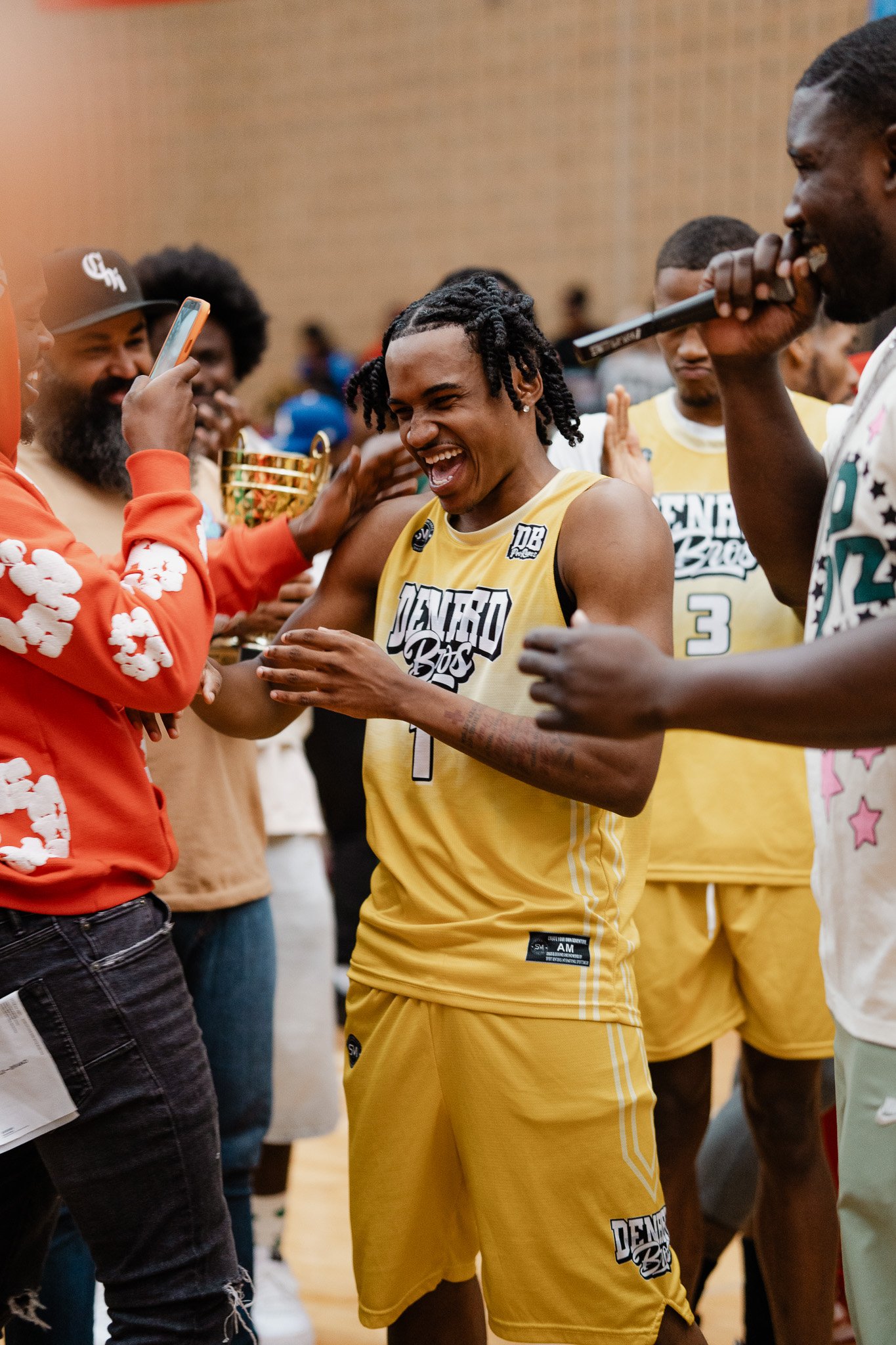 Group of basketball players celebrating during an event, with one player in a yellow jersey smiling and interacting with others.