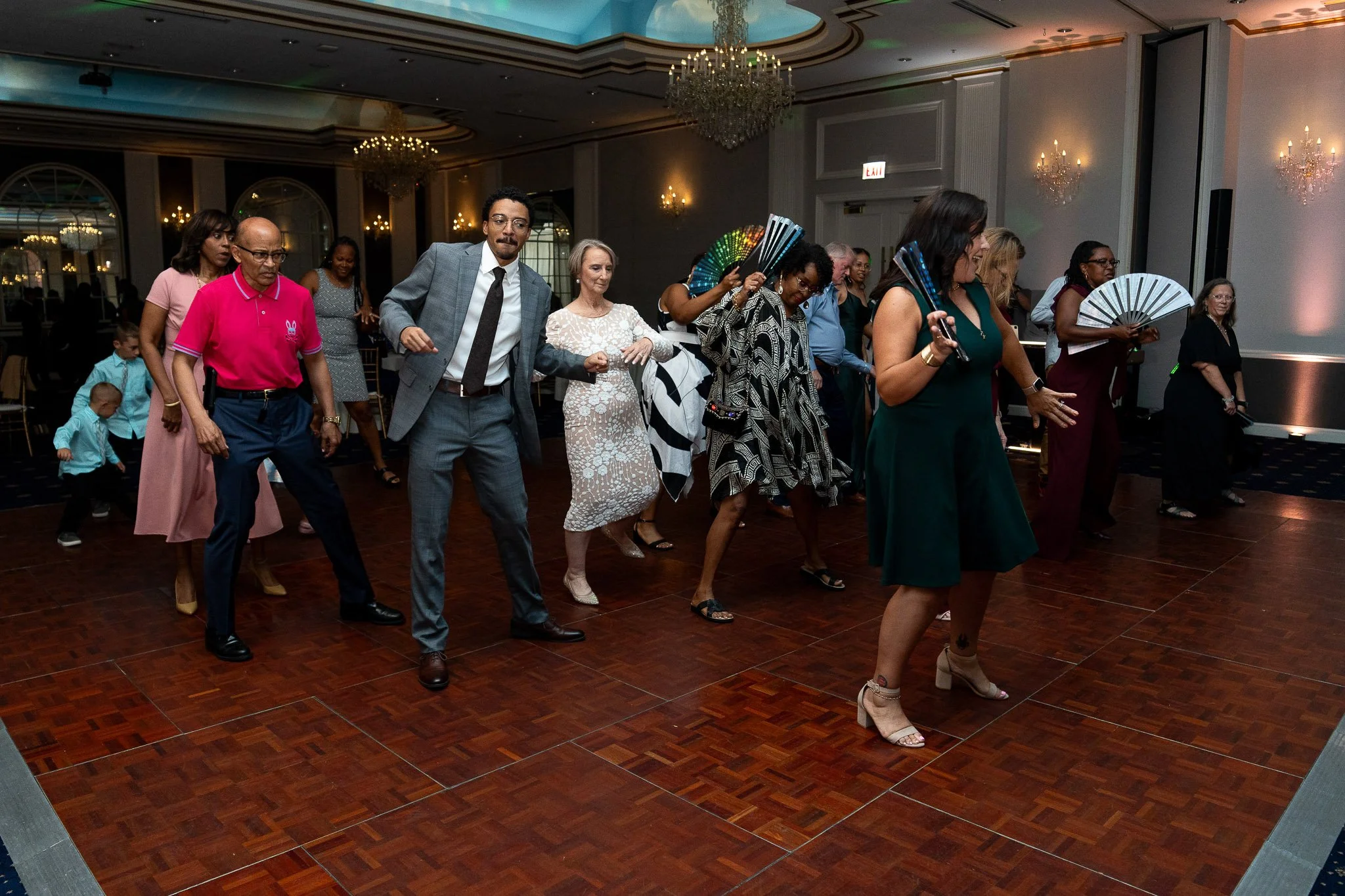 People dancing at a formal indoor event in a ballroom with chandeliers and elegant decor.
