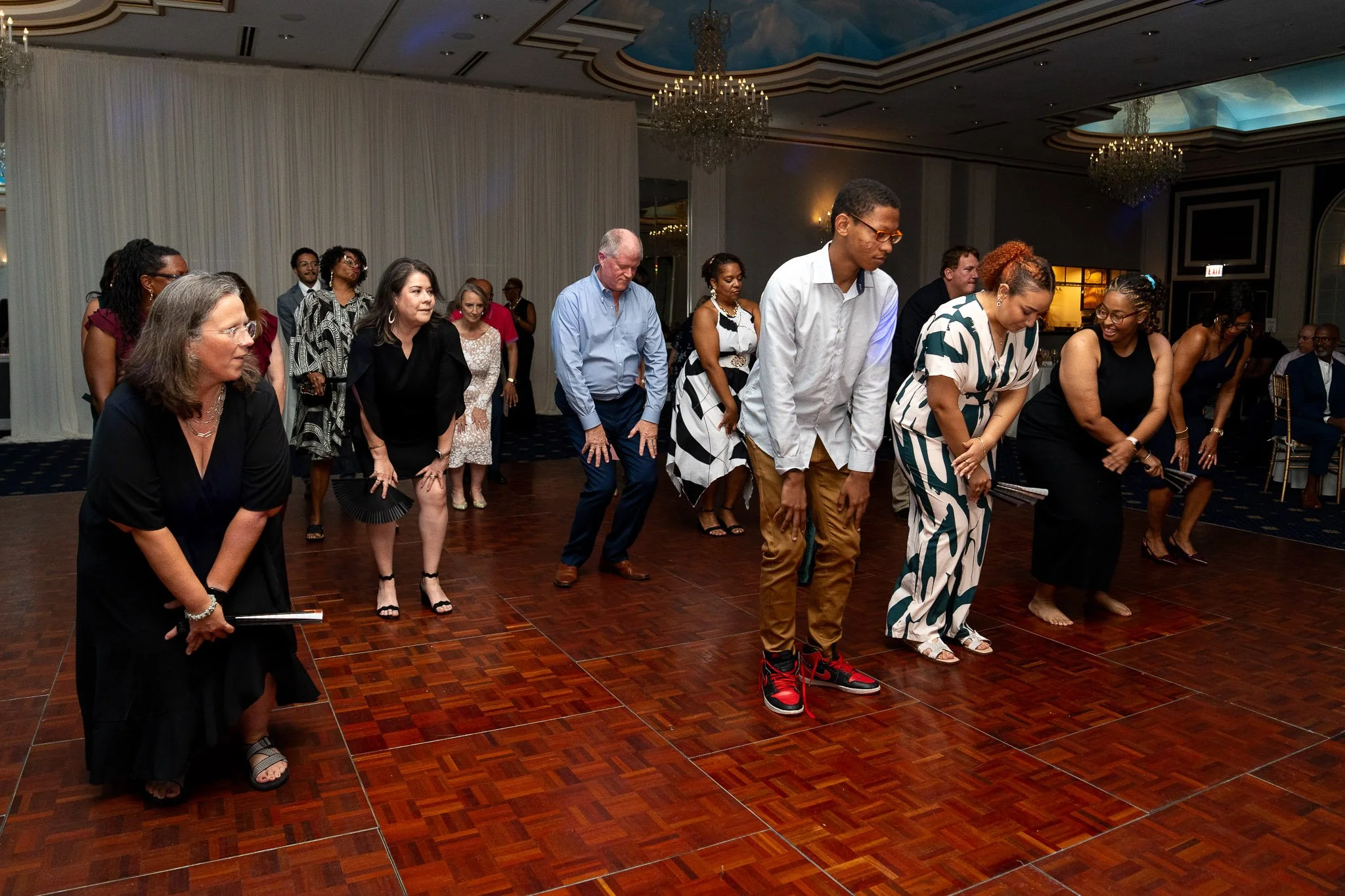 Group of people dancing together on a wooden dance floor at an indoor event or celebration.