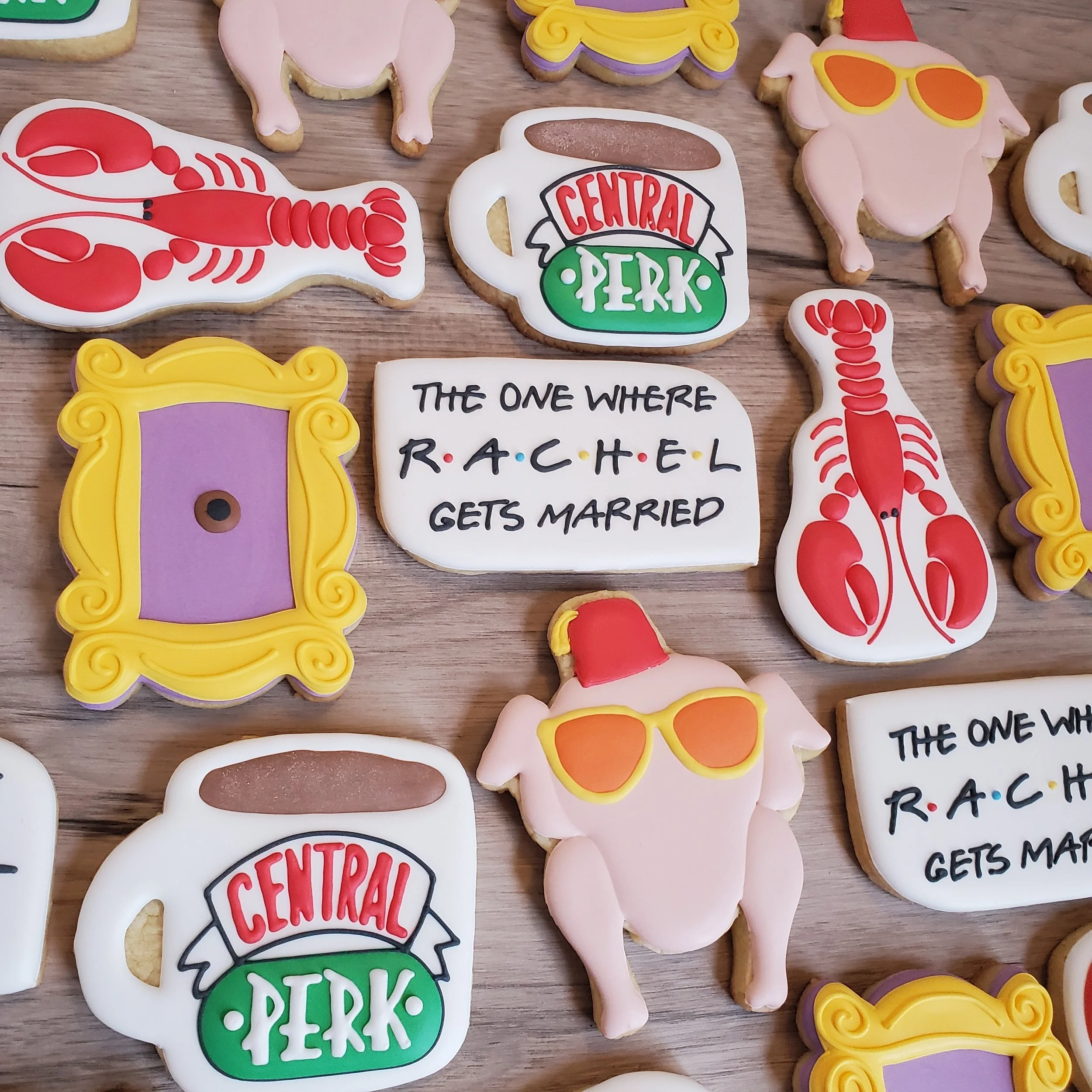 Decorated cookies themed around the TV show 'Friends', featuring Central Perk coffee mug, lobster, turkey with sunglasses, empty picture frame, and a quote about Rachel getting married.