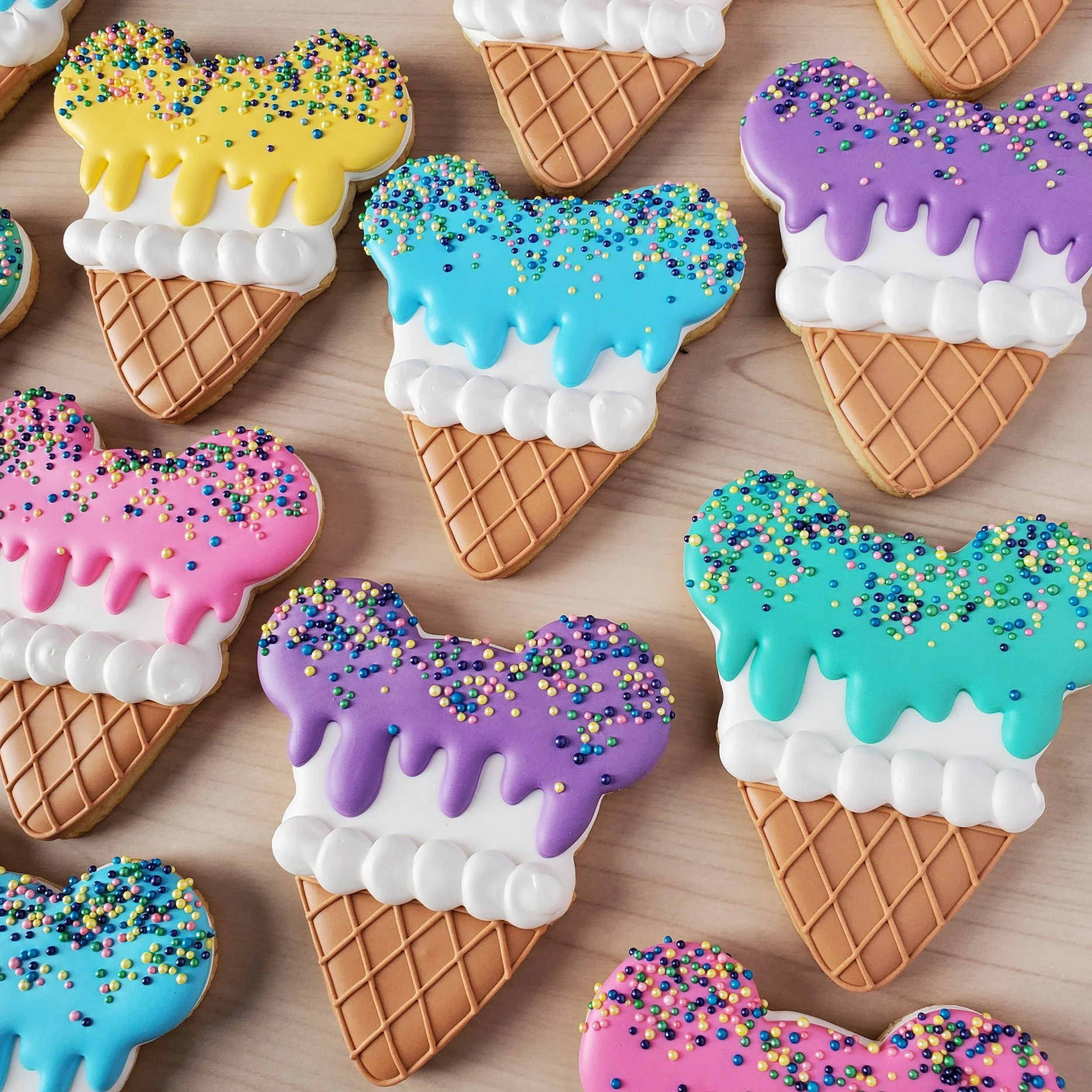 Colorful ice cream cone cookies with drip frosting and multicolored sprinkles on a wooden surface.