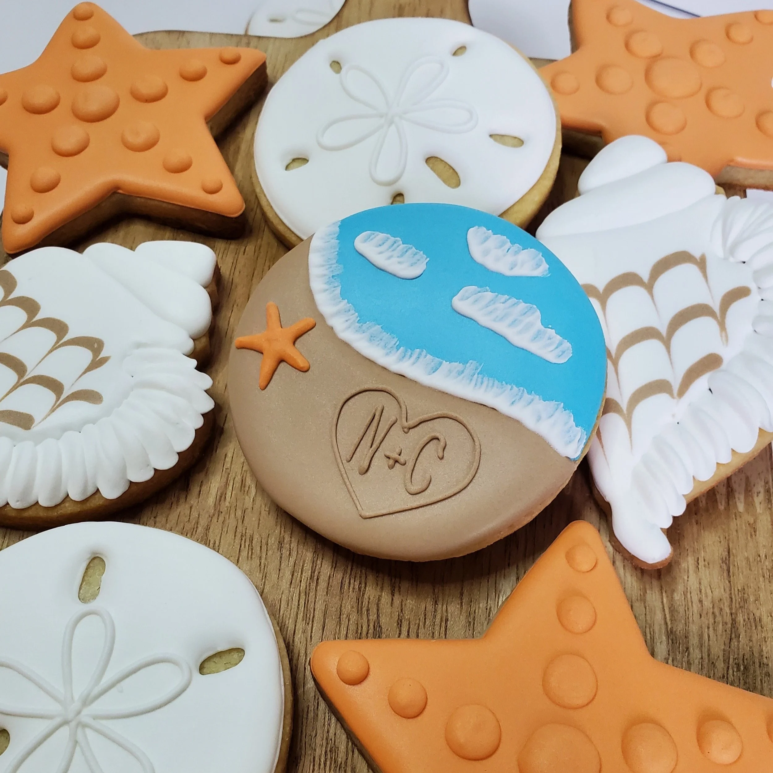 Decorative cookies with beach and starfish themes, including a star-shaped cookie, round cookies with white and brown icing, and a cookie with blue icing and sandcastle drawings on white icing.