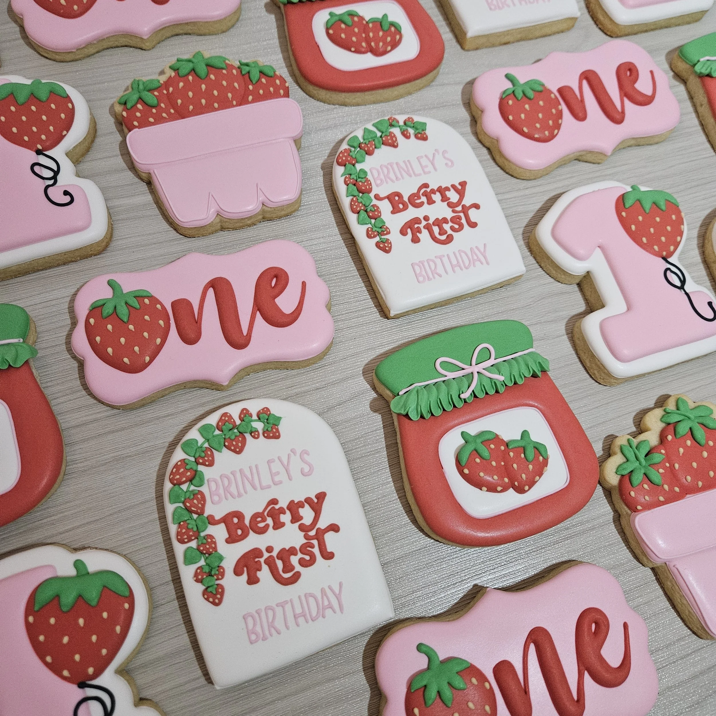 Decorated cookies with strawberries and birthday messages, featuring pink, white, red, and green icing designs.