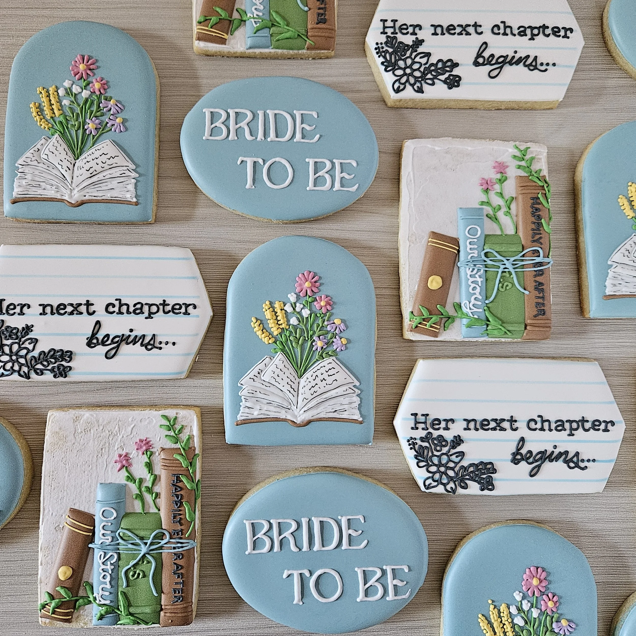 Decorative cookies with themes of books and graduation, including messages like "BRIDE TO BE" and "Her next chapter begins" with designs of books, flowers, and graduation scrolls.