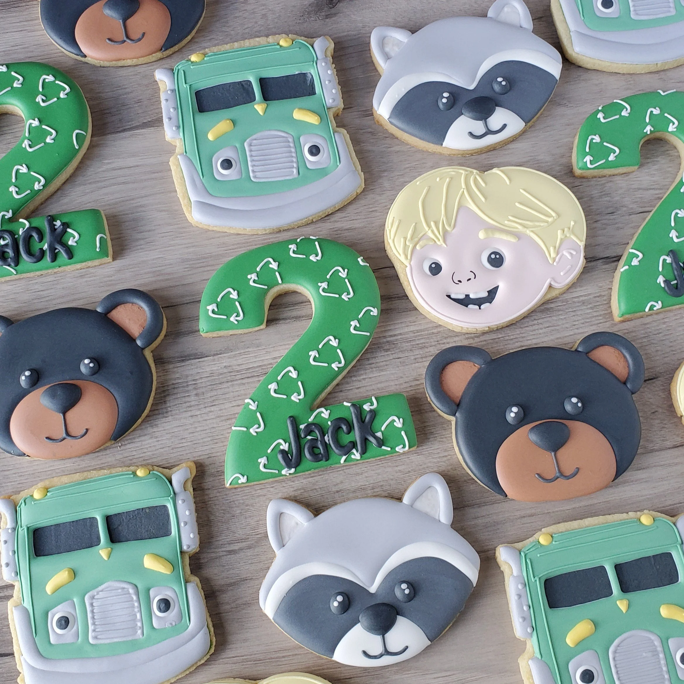 Decorative cookies featuring cartoon characters including bears, raccoons, and trucks, with a green number 2 cookie decorated with white recycling symbols and the name Jack.