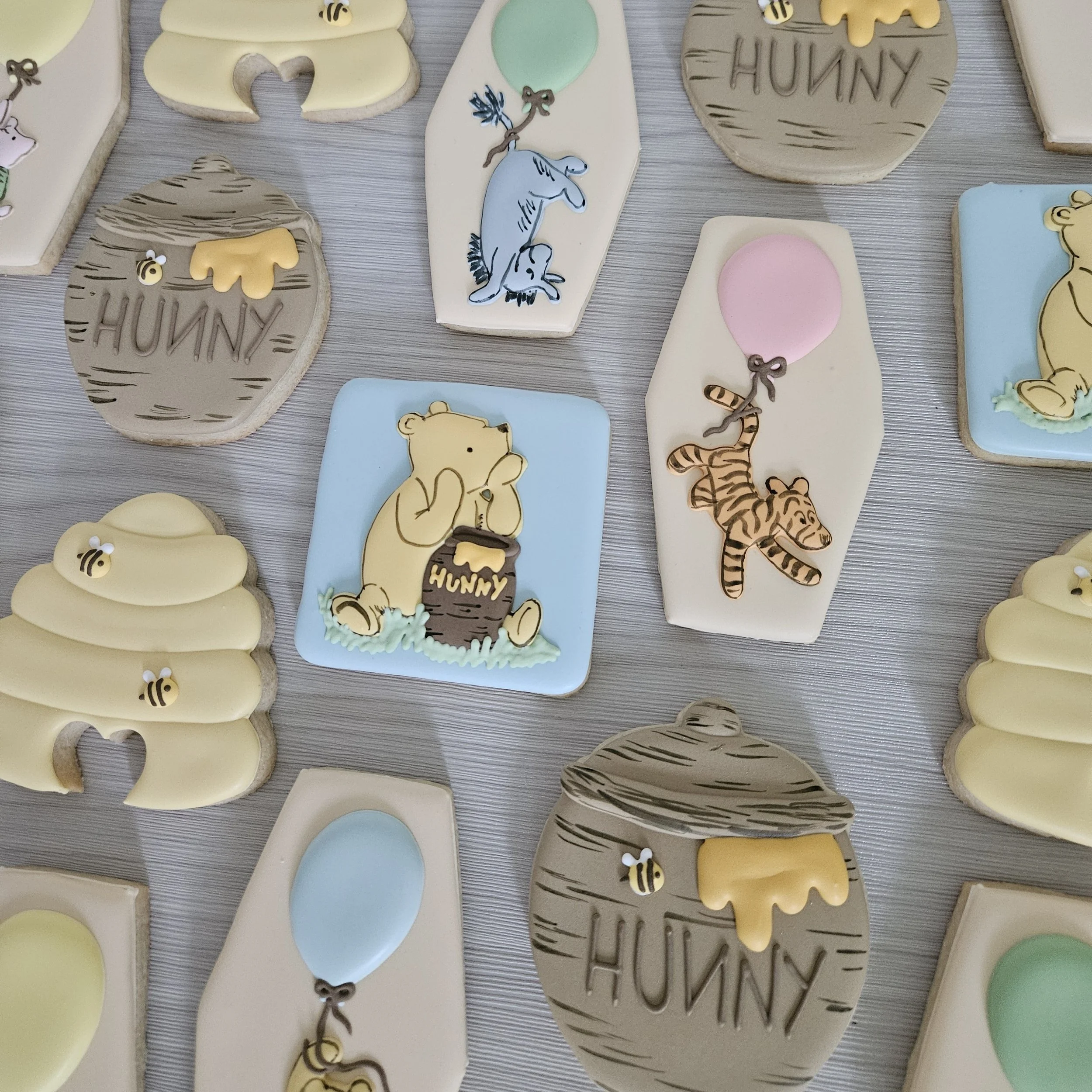 Assorted decorated cookies with honey bee, honey jar, and animal designs, including bears, elephants, and tigers, on a light gray surface.