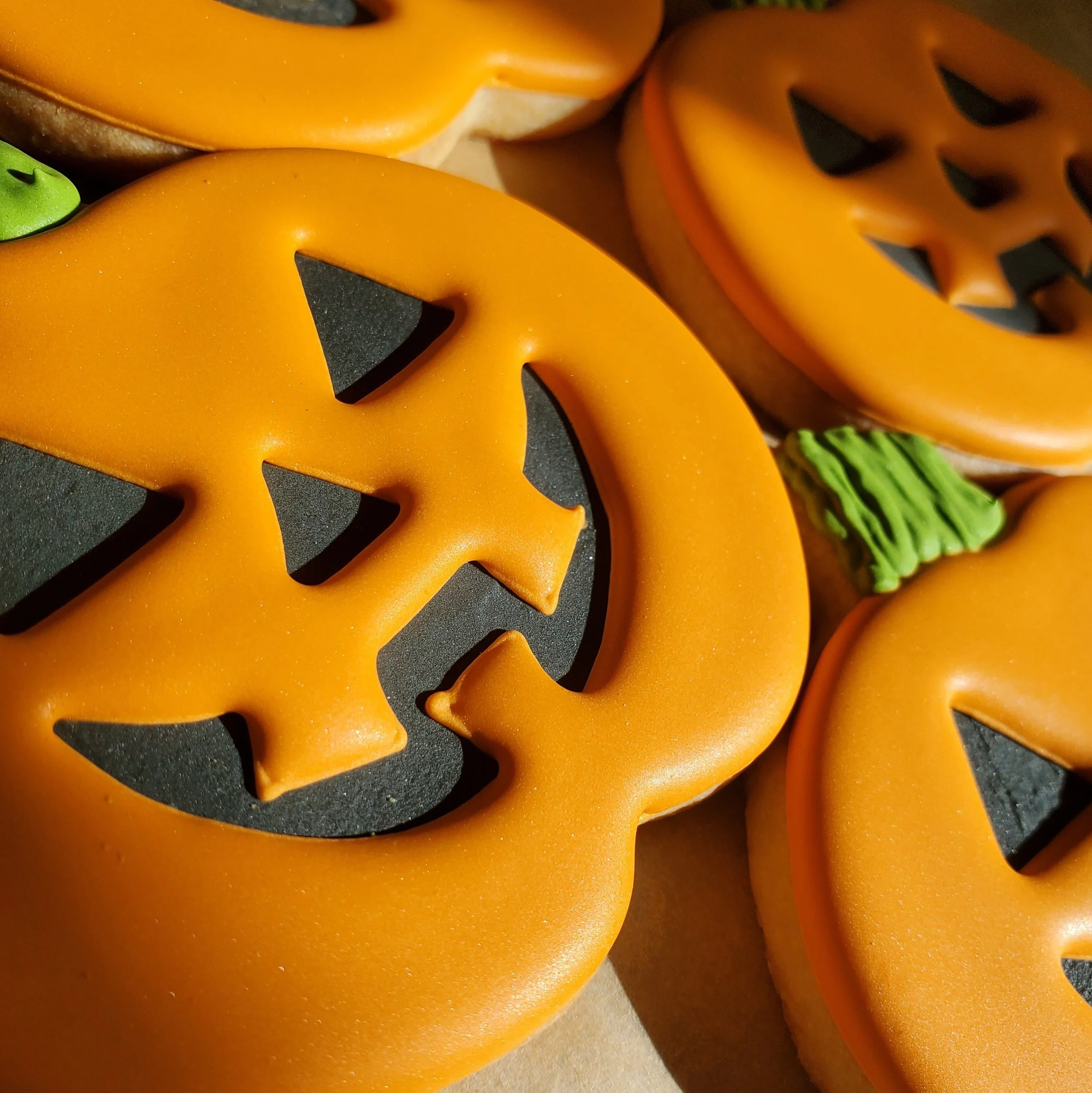 Close-up of Halloween-themed cookies decorated as jack-o'-lantern faces with orange icing, black eyes and mouths, and some with green icing stems.