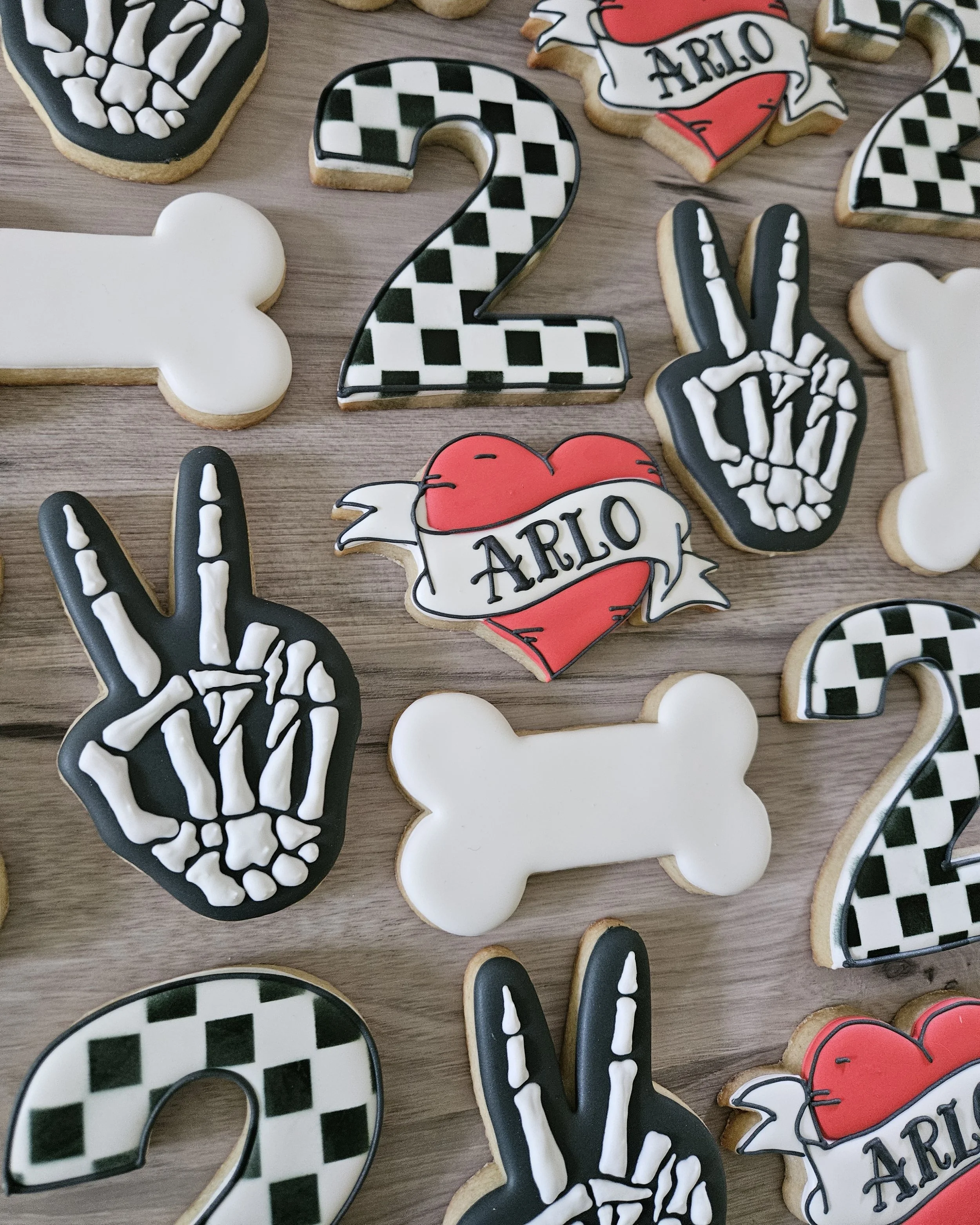 Decorative cookies in black, white, and red colors with designs including peace signs, checkered patterns, bones, and the name 'Arlo' on a heart with a banner.