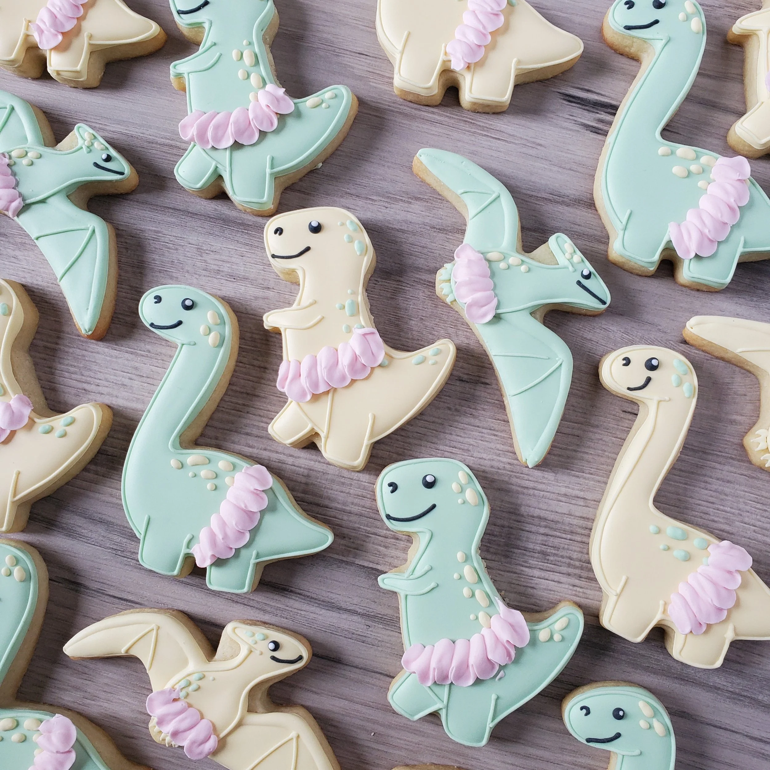 Cookies decorated as cartoon dinosaurs with pastel colors and pink frills.