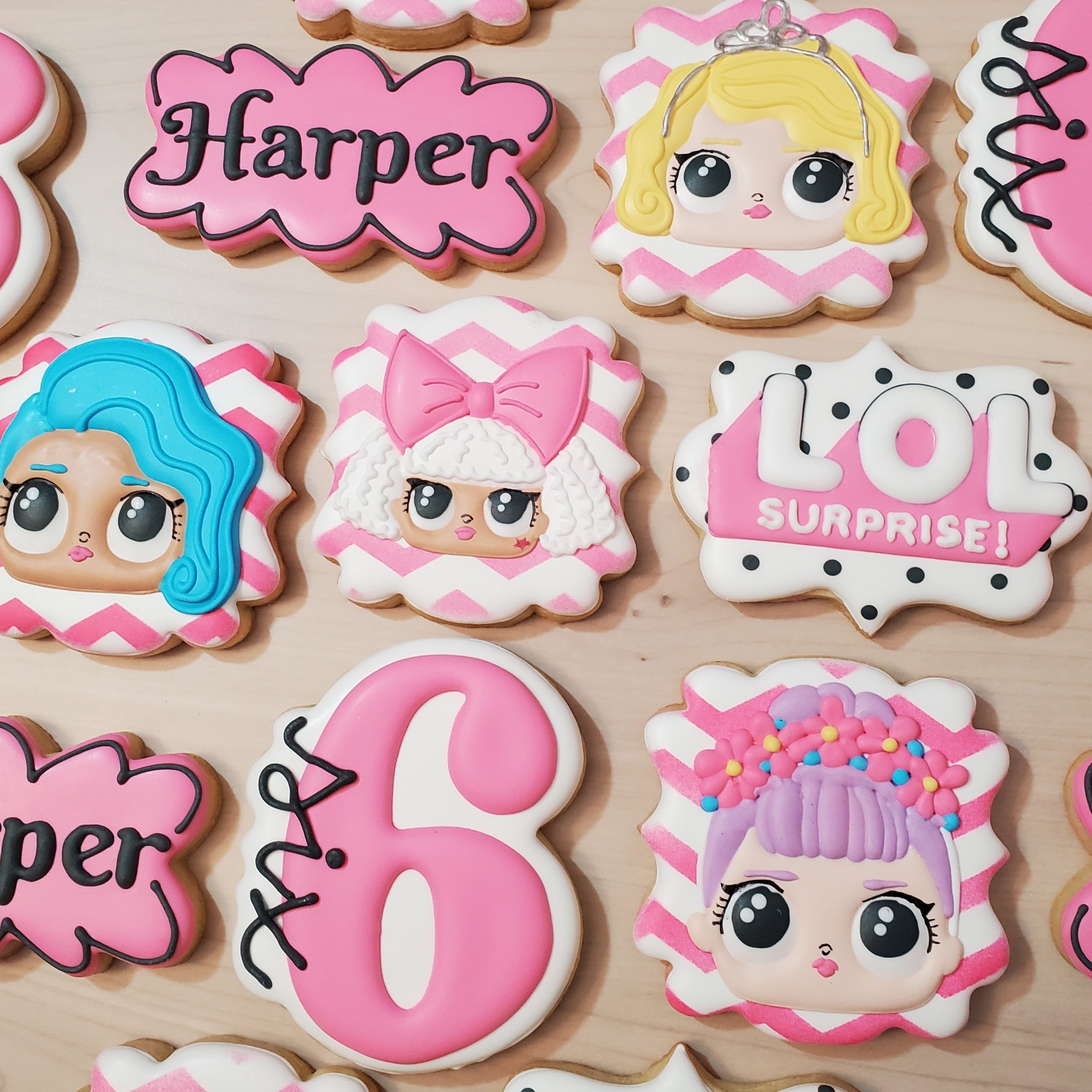 Decorated cookies with LOL doll faces, colorful hair, bows, and text, on a wooden surface.