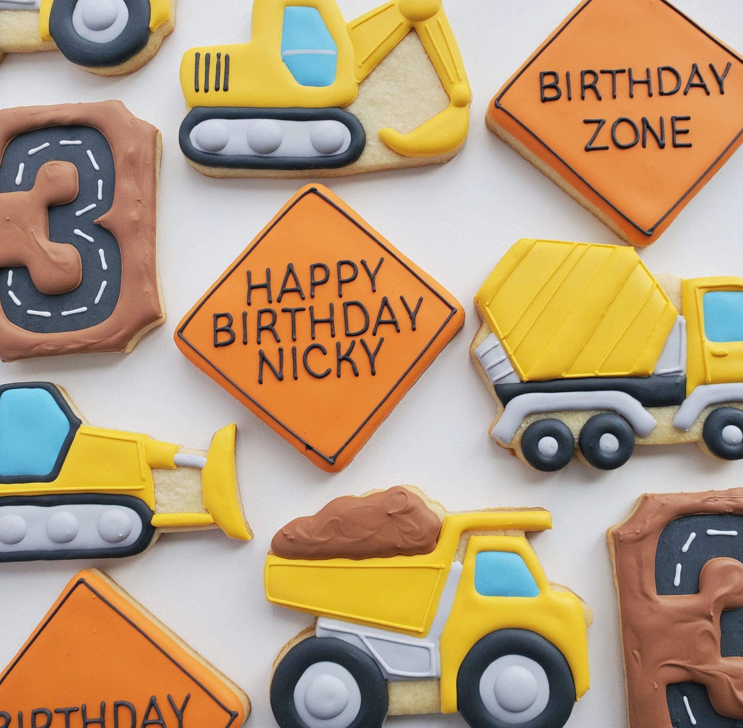 Colorful construction-themed birthday cookies with trucks, diggers, and road signs reading 'Happy Birthday Nicky' and 'Birthday Zone'.