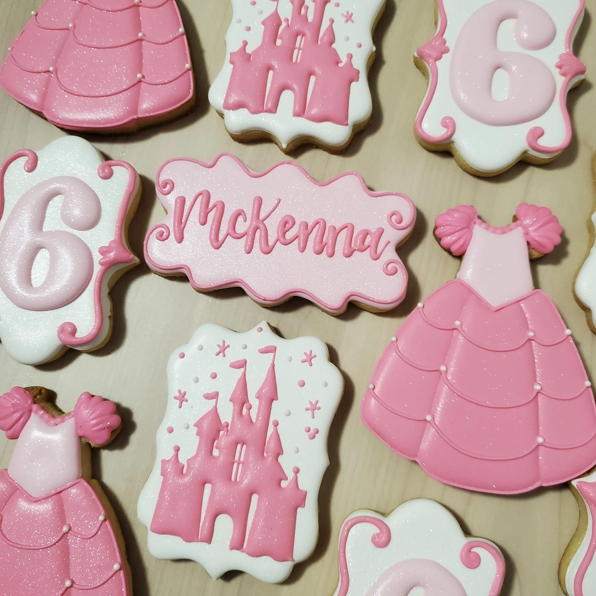 Pink and white cookies decorated for a birthday, featuring castles, a dress, and the name 'Mckenna'.