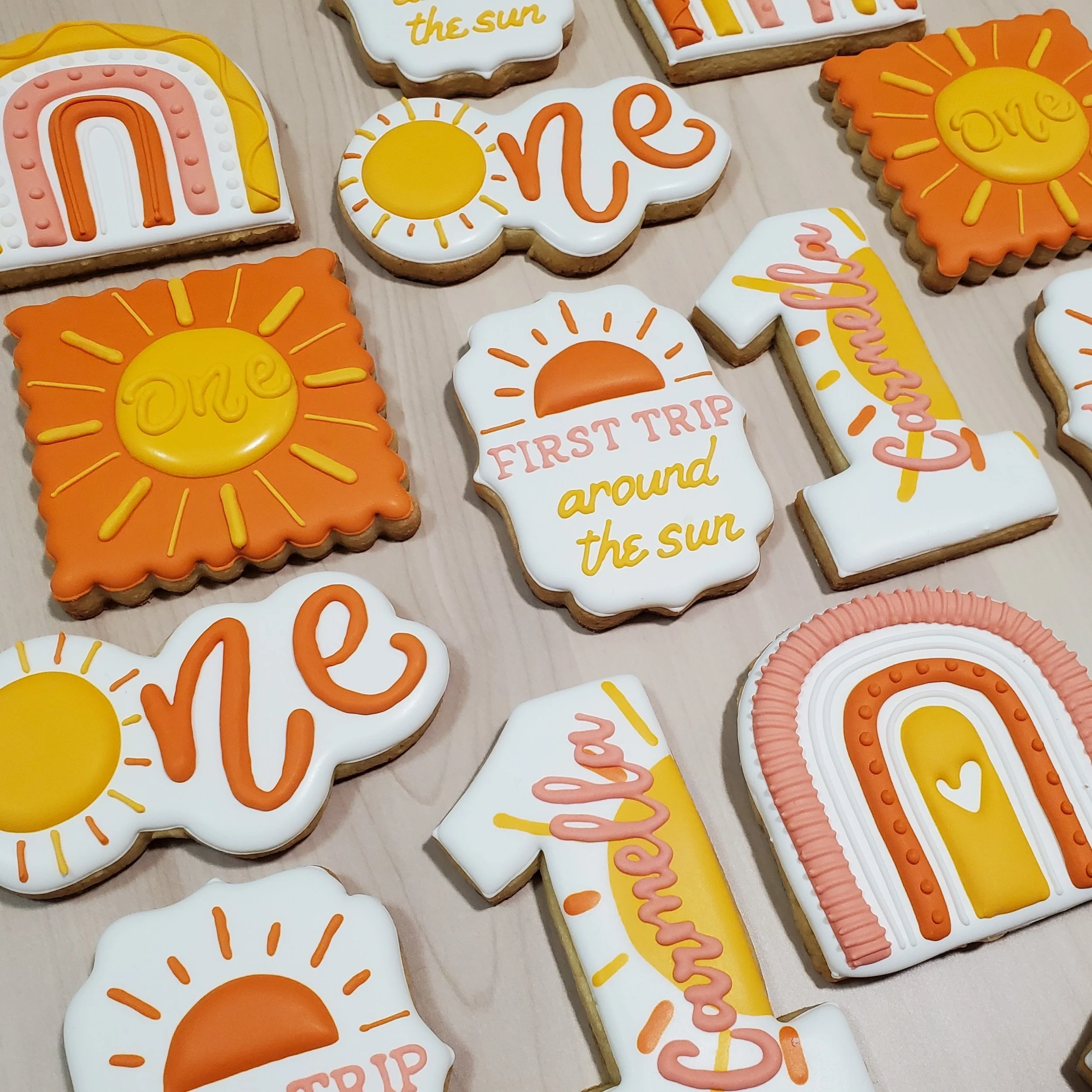 Decorative cookies with sun and travel themes, including phrases like 'First Trip around the Sun' and 'Love,' decorated in yellow, orange, and pink icing.
