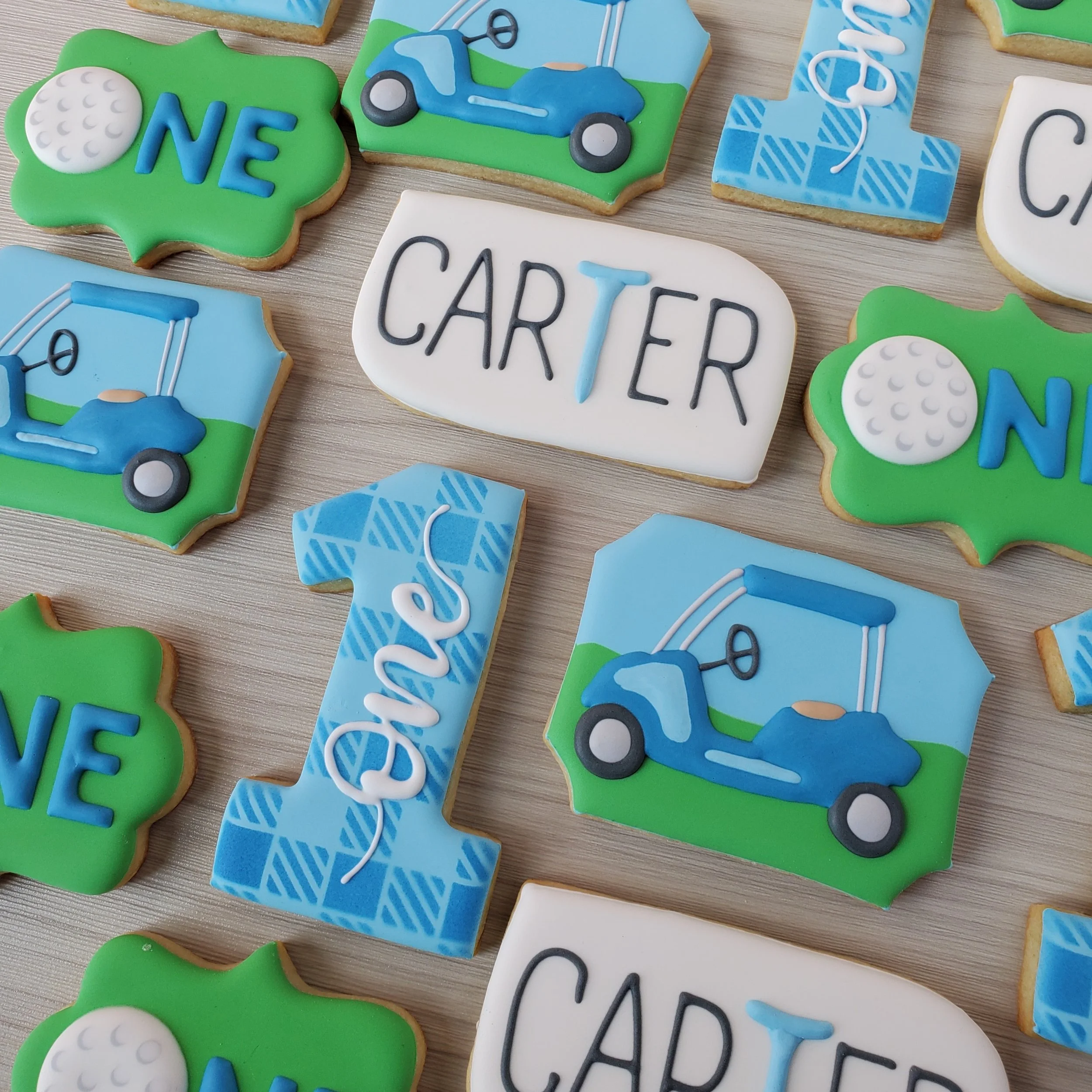 Decorated cookies for a golf-themed celebration, featuring golf balls, golf carts, and personalized names and numbers with green, blue, and white icing.
