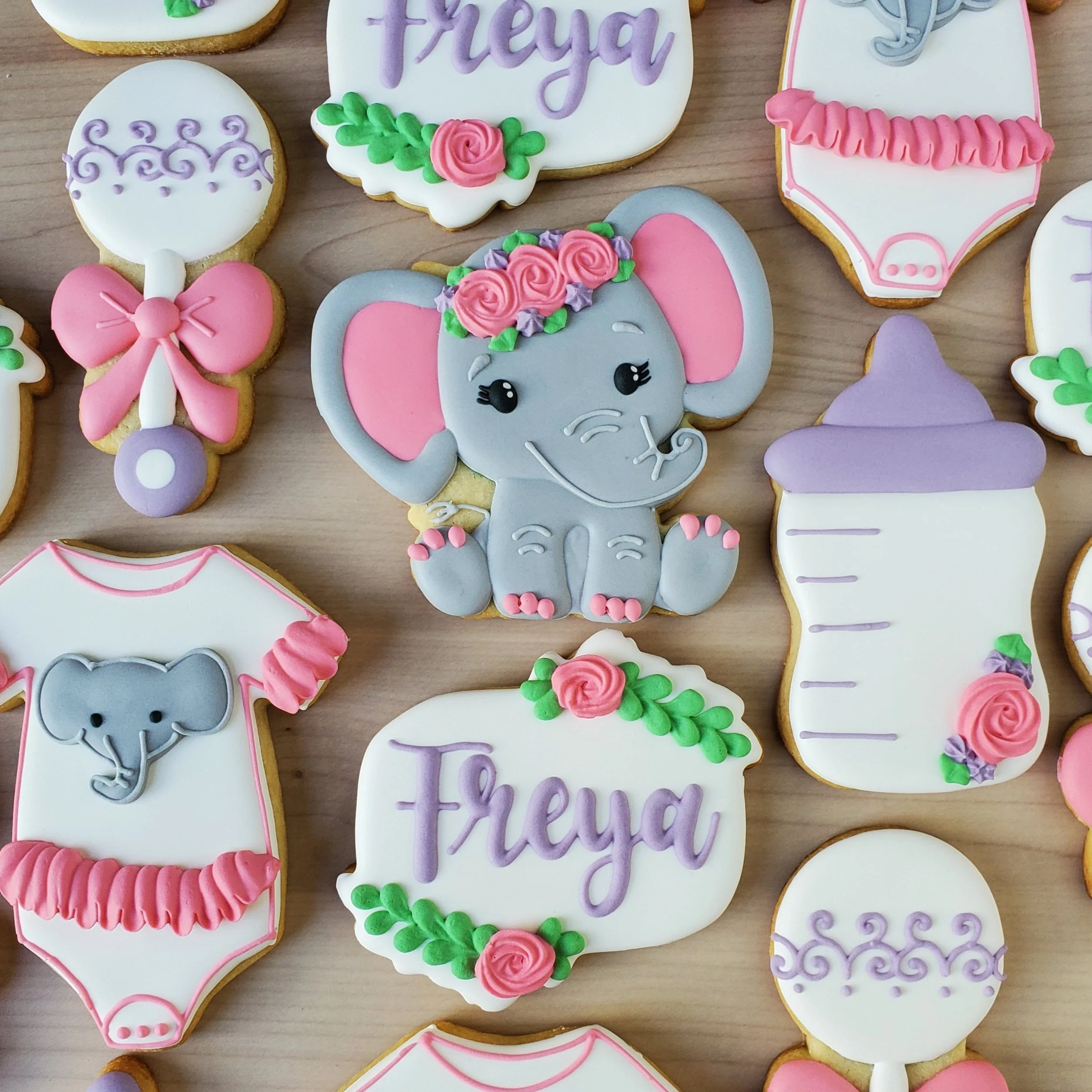 Decorated cookies featuring baby shower themes with elephants, bottles, and the name "Freya" written in purple icing, all with pastel colors and floral accents.