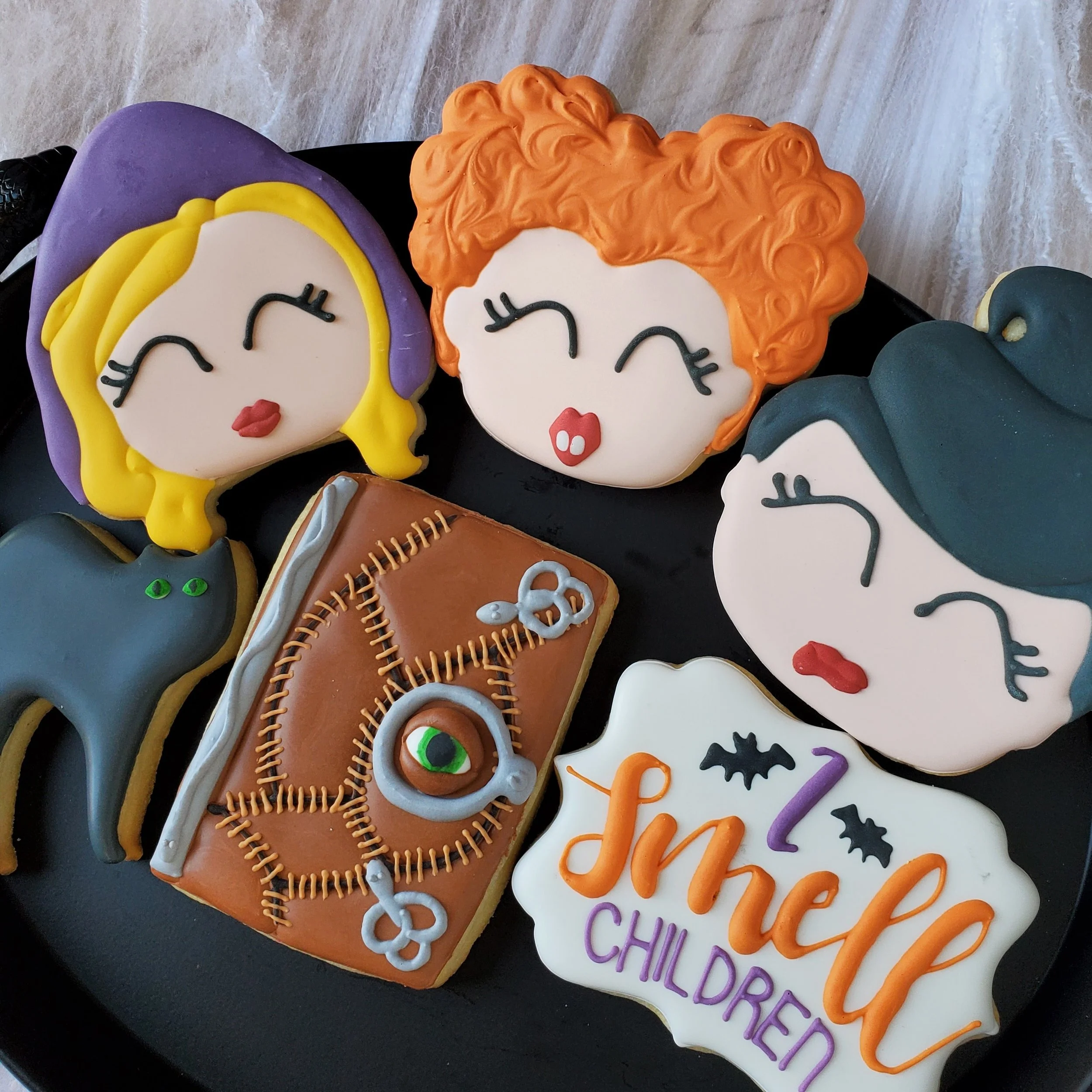 Decorative cookies with Halloween and friendship themes, including characters with different hair colors, a black cat, spooky book, and "I smell children" text