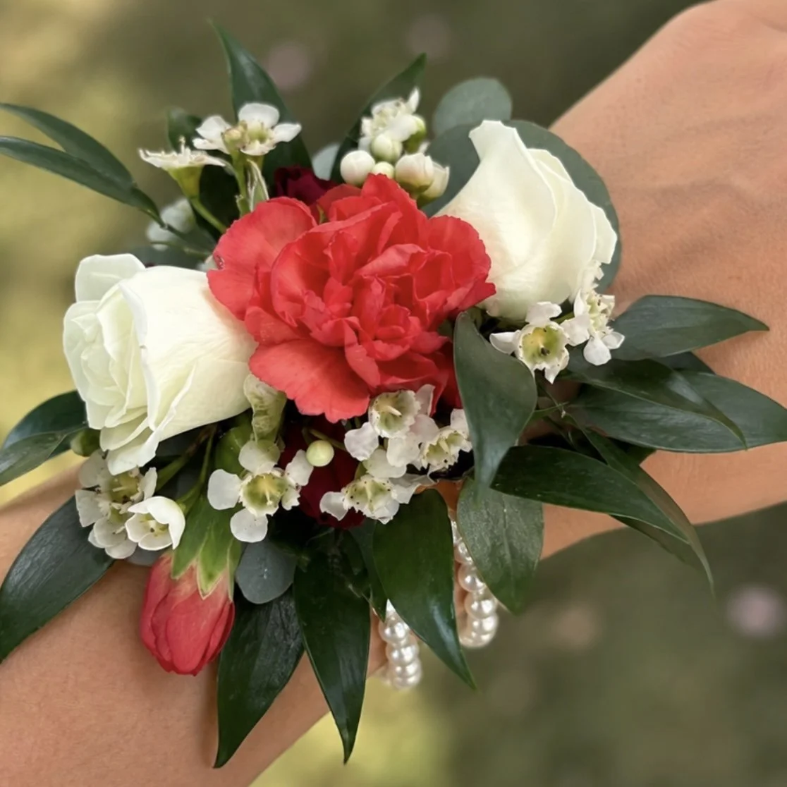 Bouquet of three orange roses and one cream-colored rose, decorated with a sparkly rhinestone band, greenery, black and white ribbons, wrapped in tulle and mesh fabric.