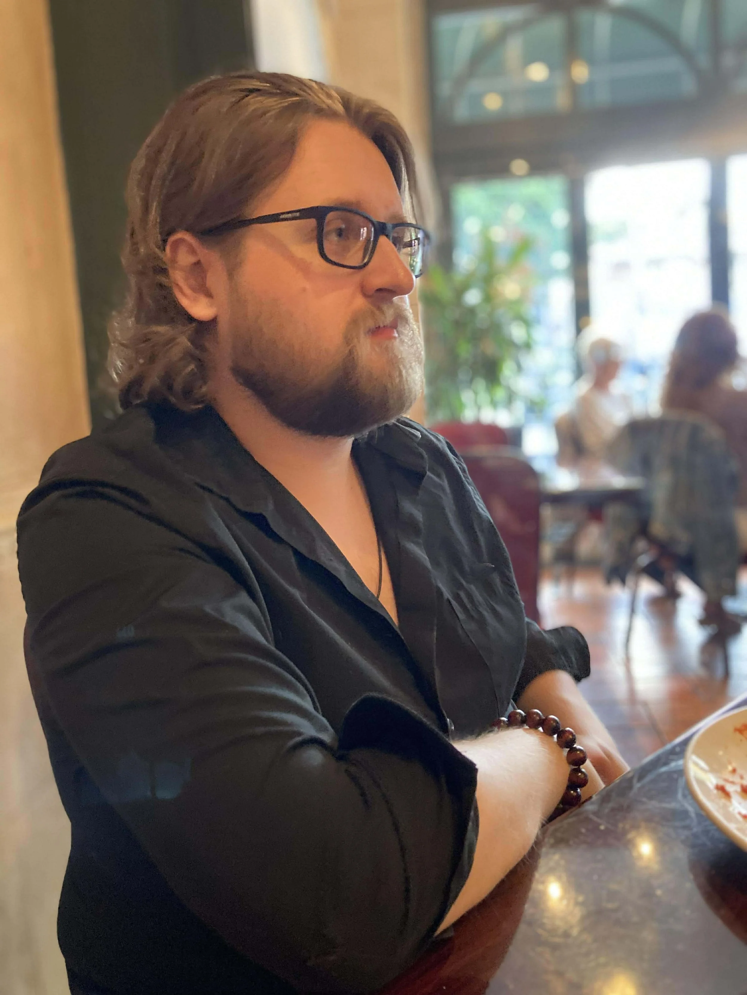 A man with glasses, long hair, and a beard sitting at a restaurant table.