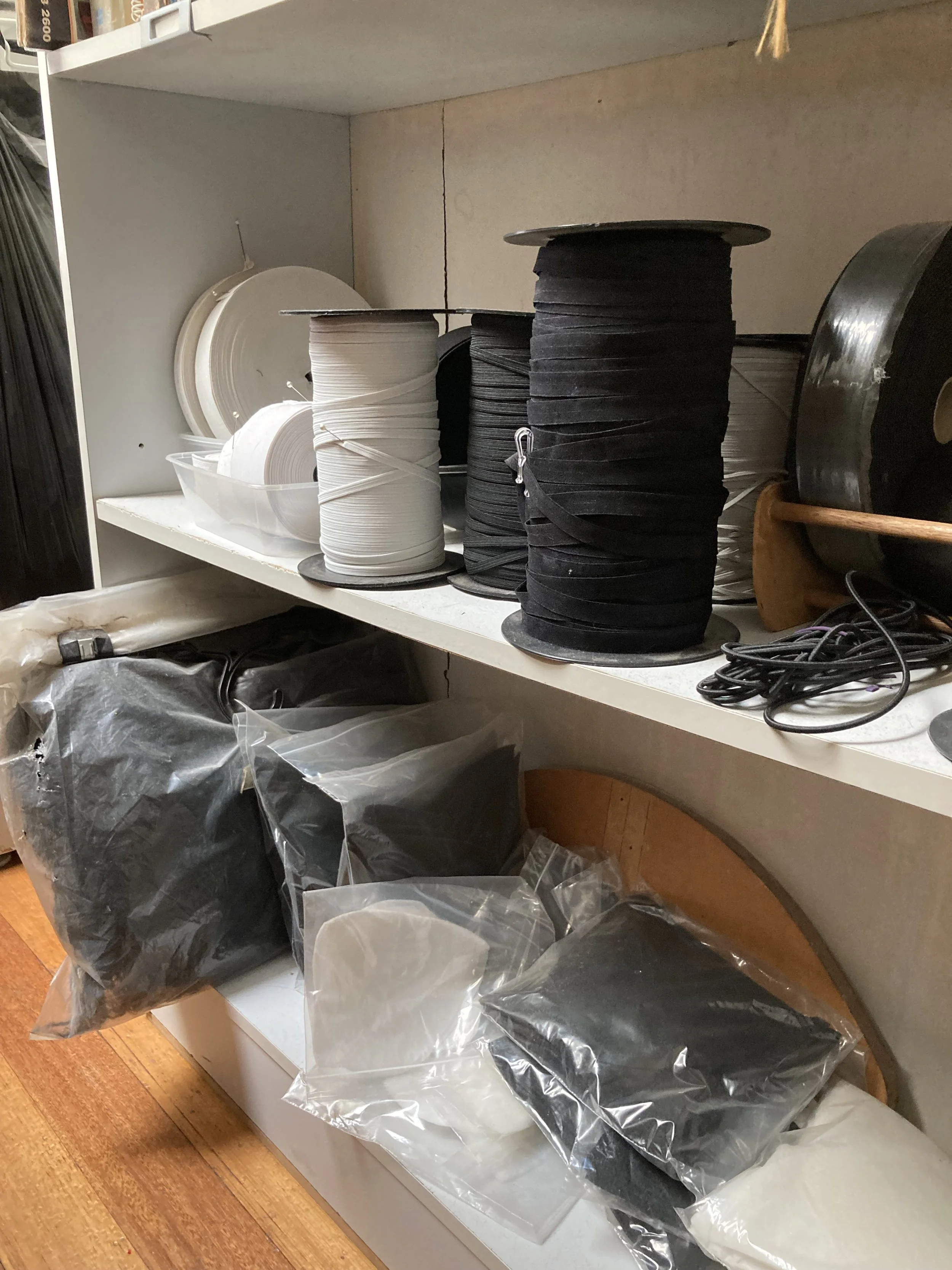 Shelves with rolls of black and white fabric, containers, cords, and plastic bags filled with various black and white materials.