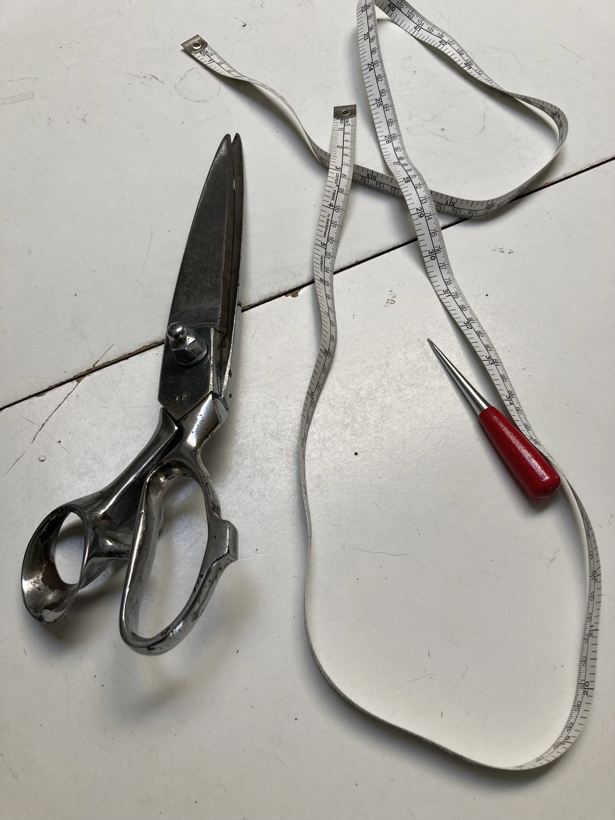Sheet metal scissors, a measuring tape, and a seam ripper on a white surface.