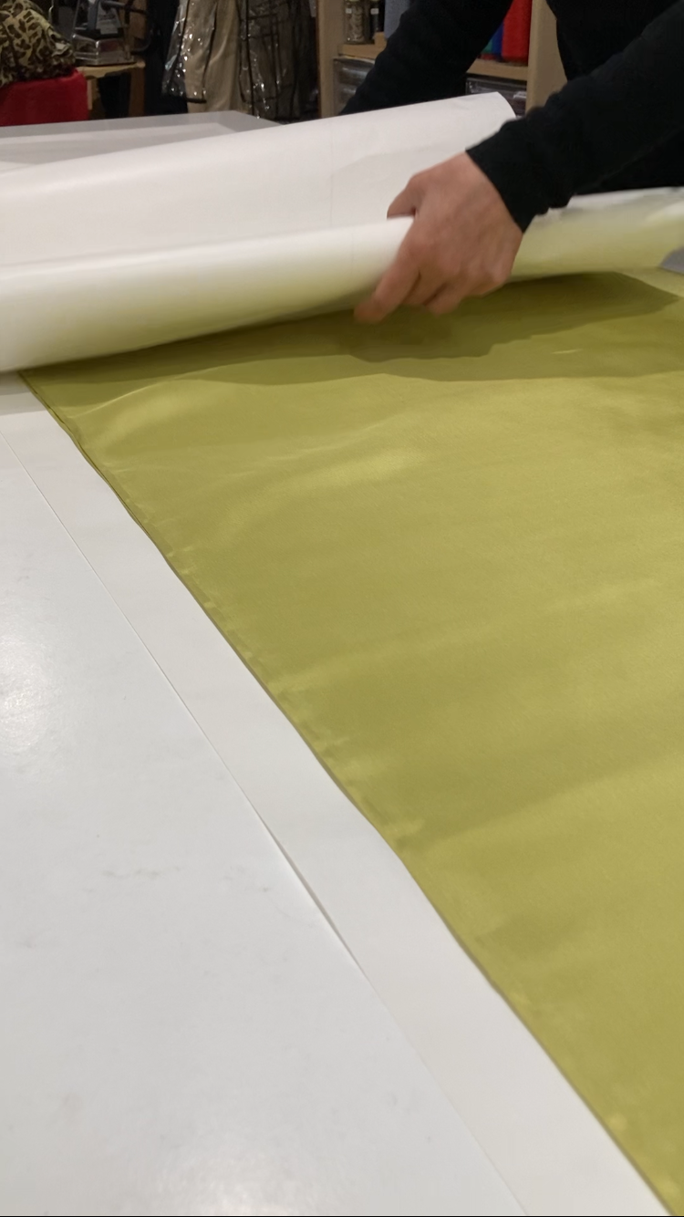 A person unrolling a roll of white paper onto a table with green fabric.