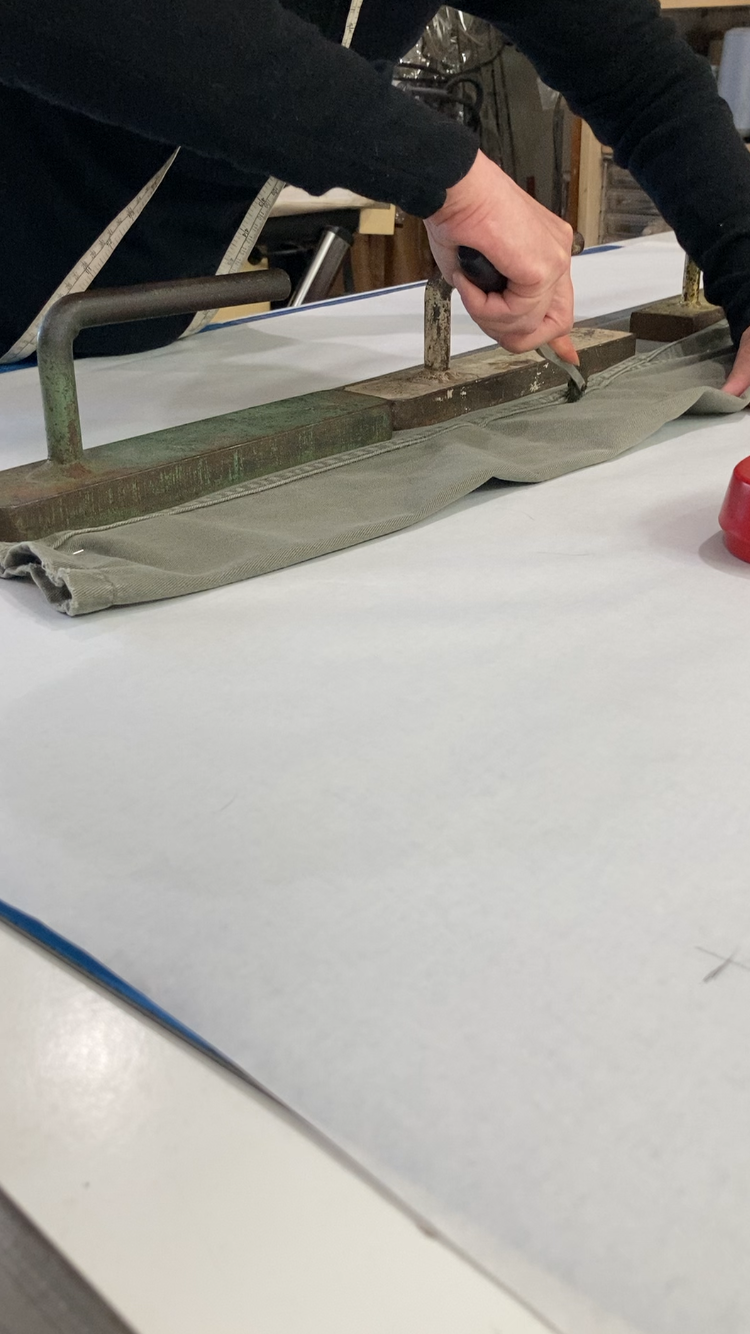 Person using a tool to press or shape fabric on a worktable in a workshop or sewing room.