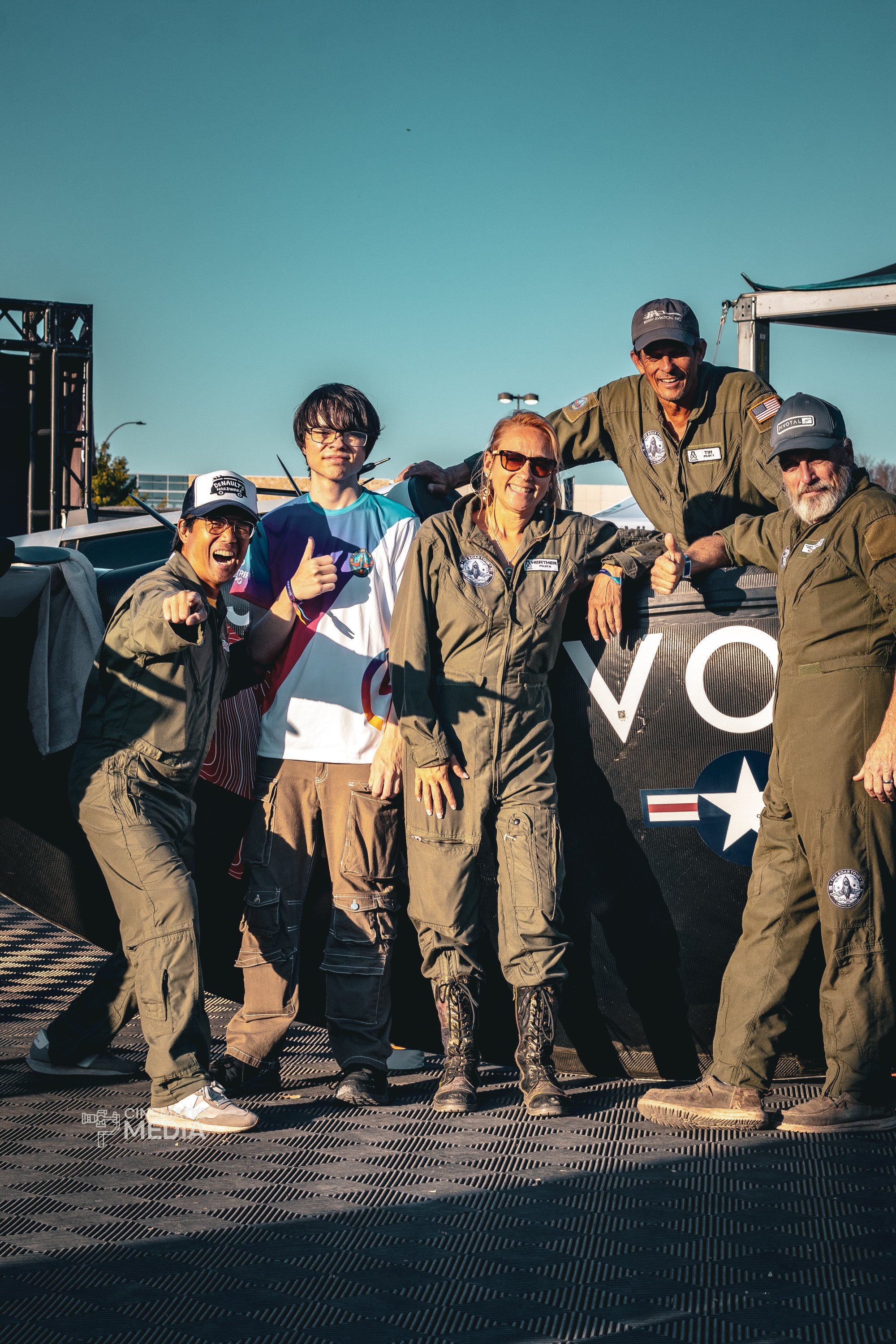 Heather Chirtea and her team in military or astronaut-style jumpsuits smiling and posing outdoors under a clear blue sky.